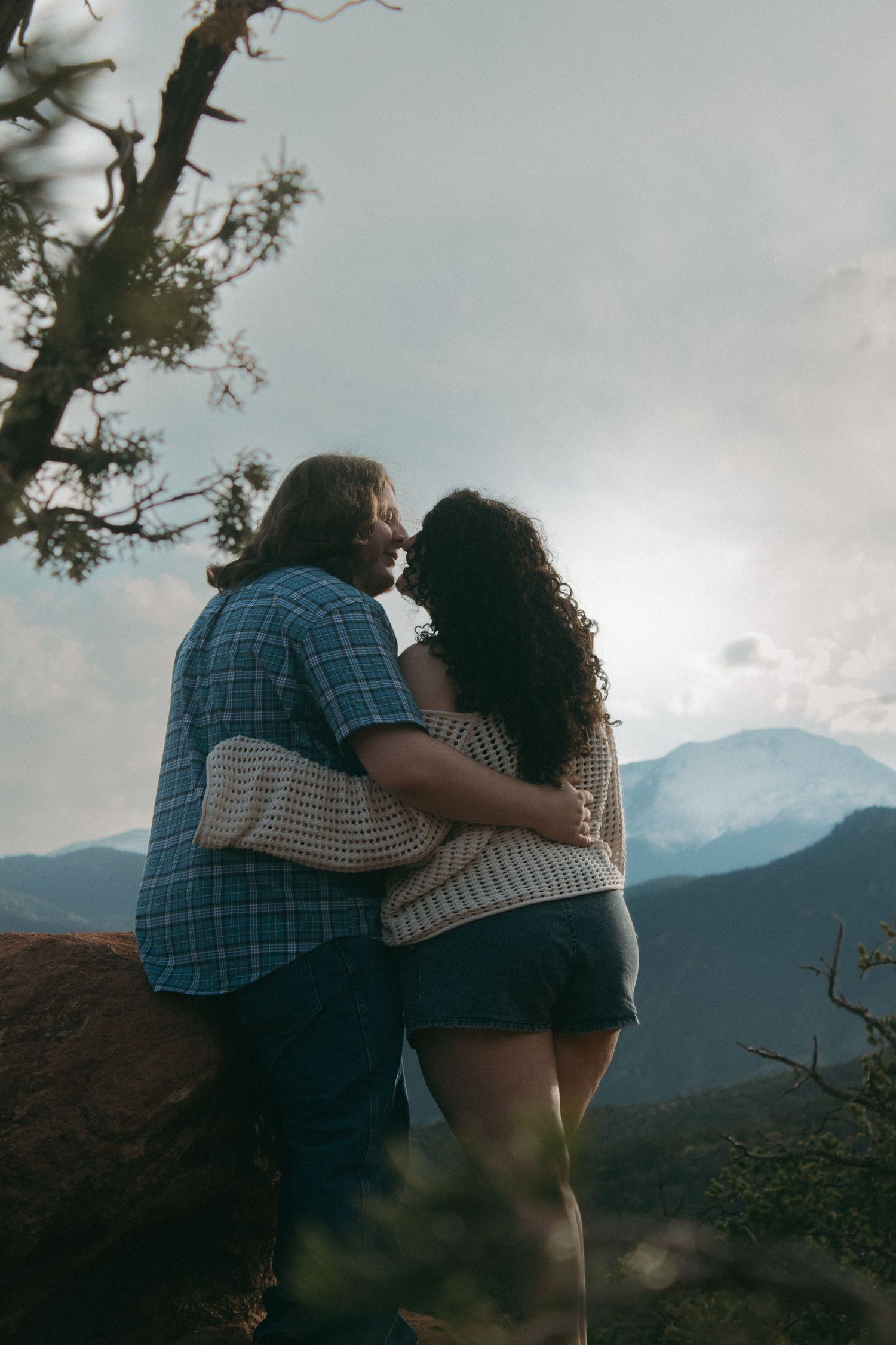 A couple shares an intimate moment against a backdrop of misty mountains during sunset.