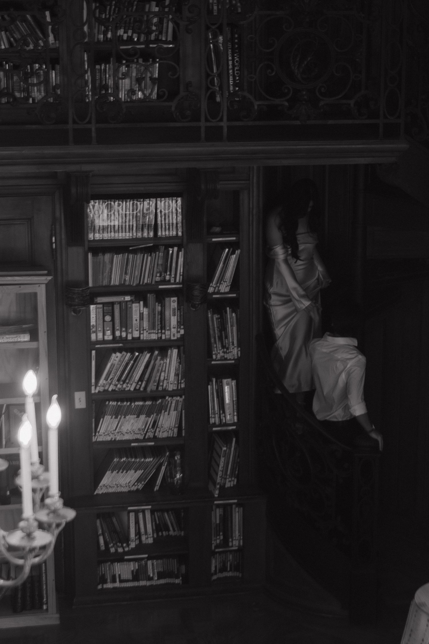 Dimly lit library interior with bookshelves and candlelight creating a moody atmosphere.