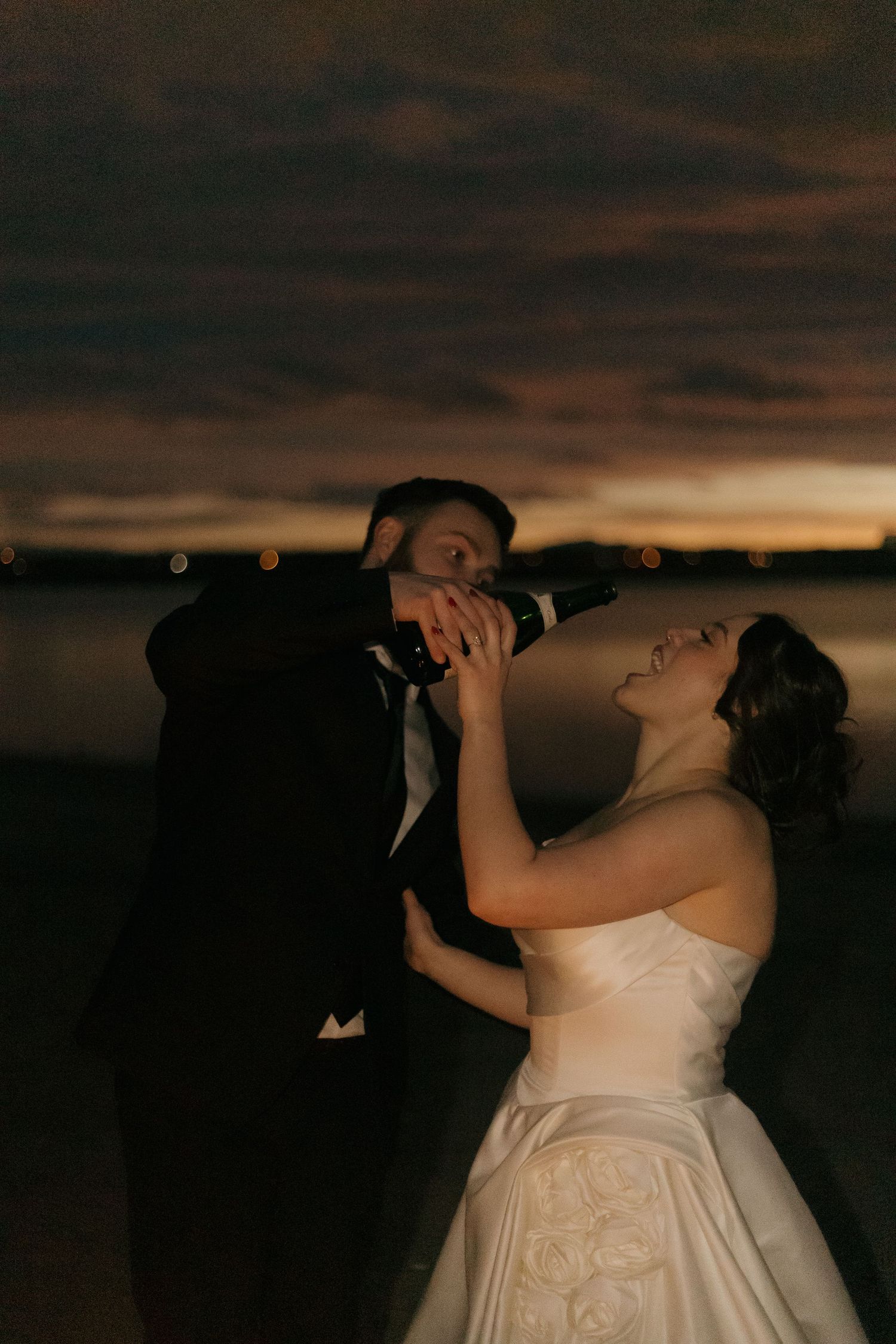 A dramatic sunset photo of a couple dancing together at their wedding reception.