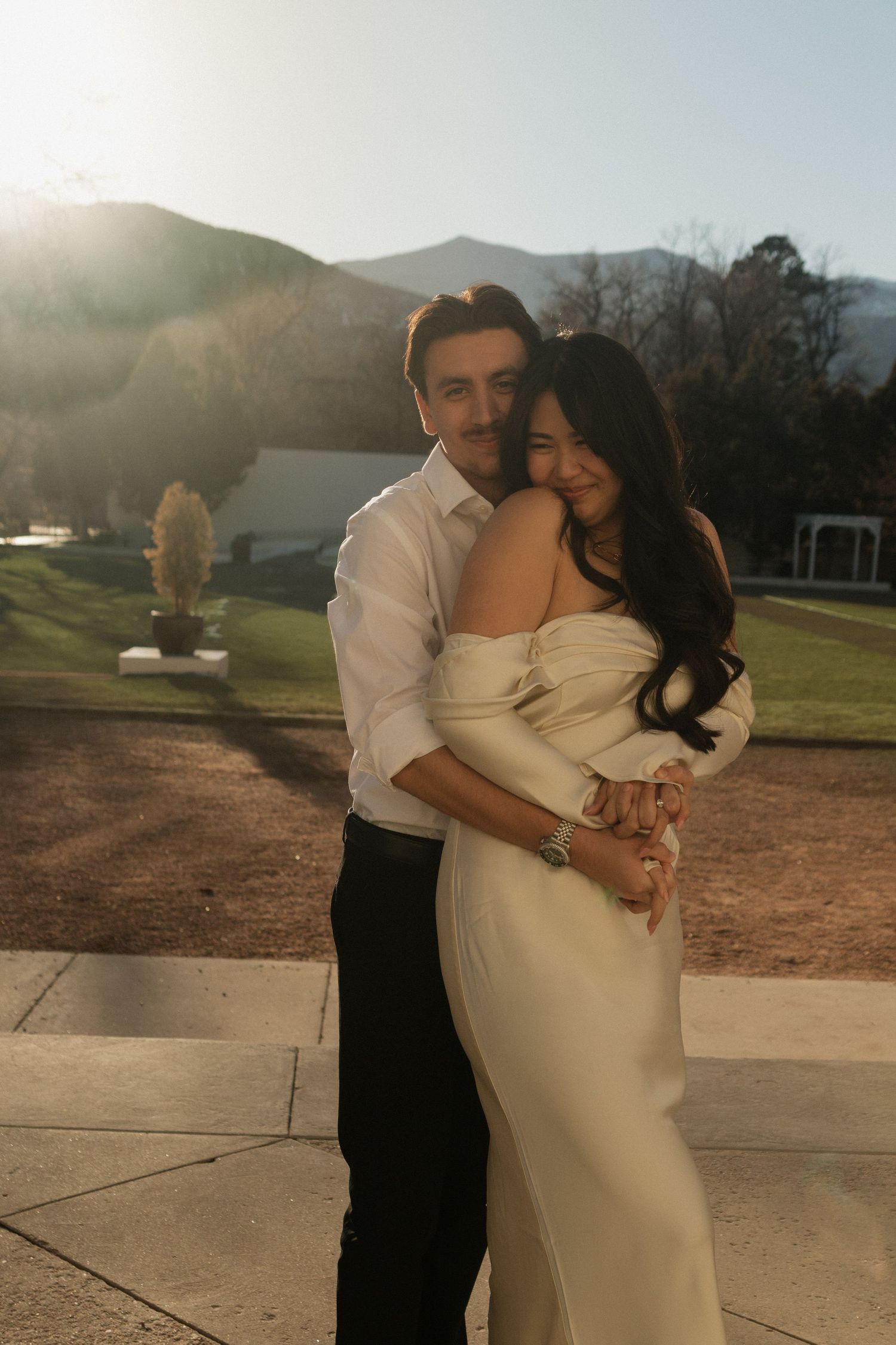 A romantic sunset embrace captured outdoors with mountains in the background.