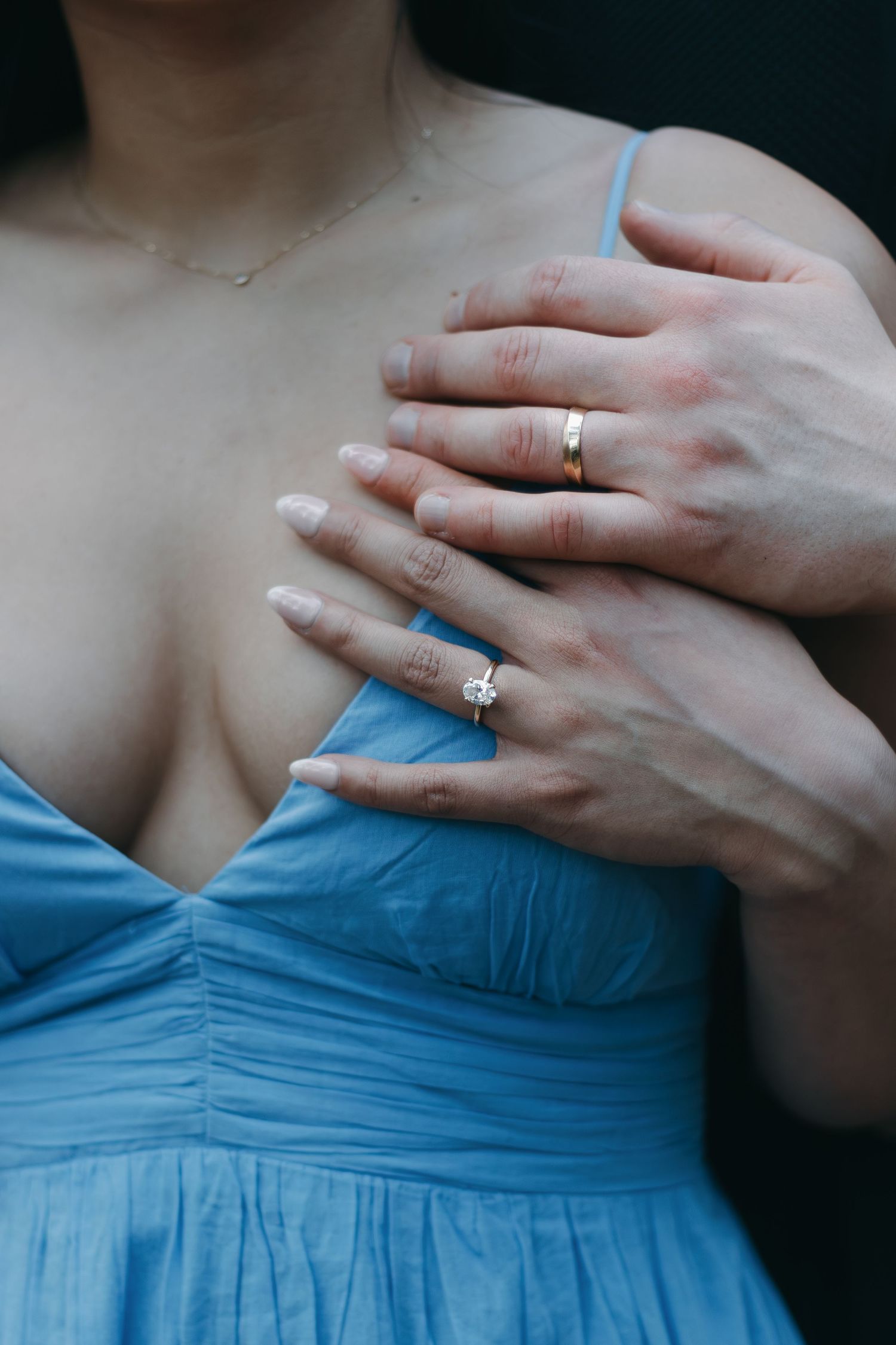Close up of hands wearing wedding rings against a light blue dress.