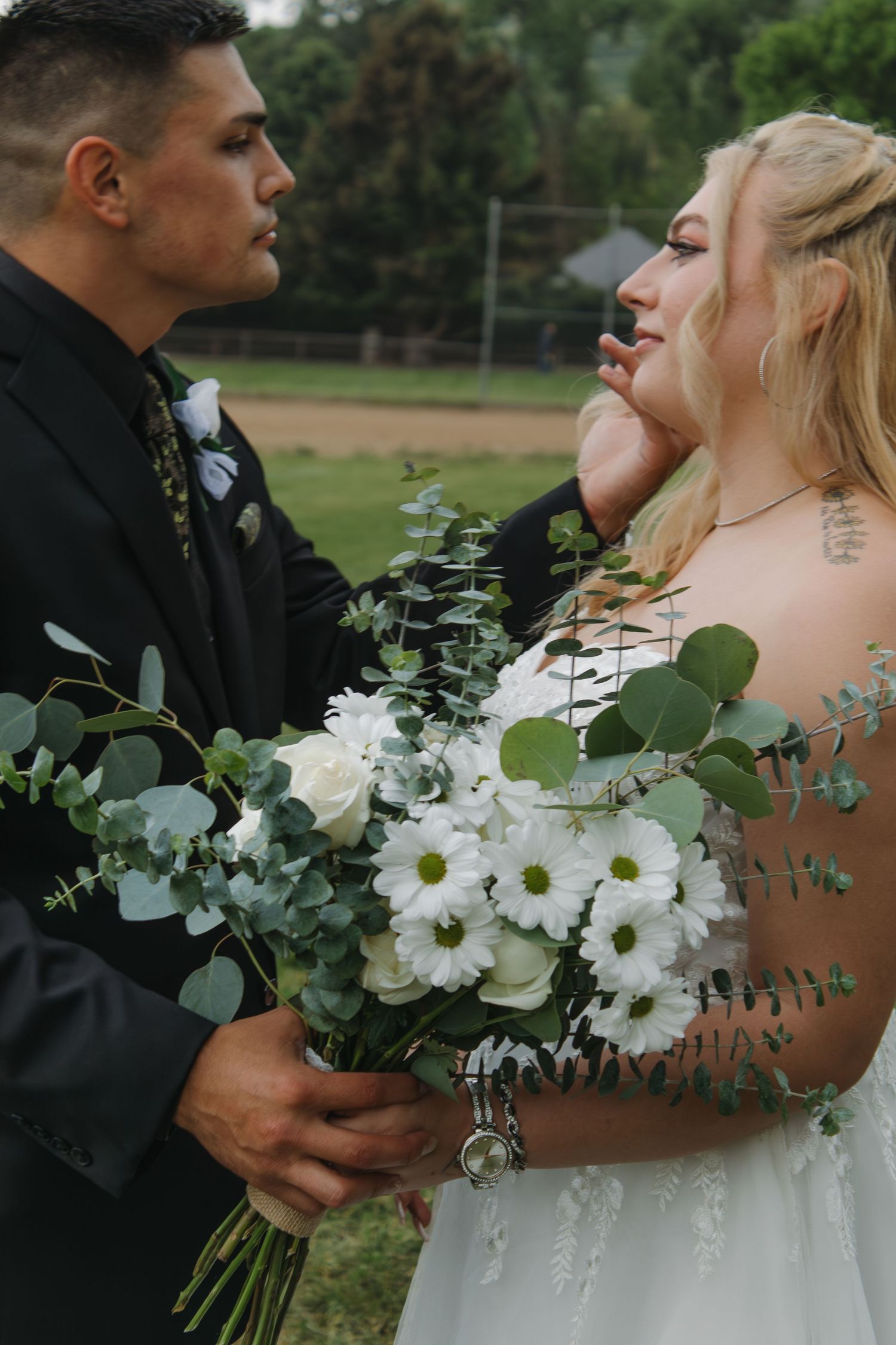 Close-up of couple sharing intimate moment with white and green wedding bouquet.