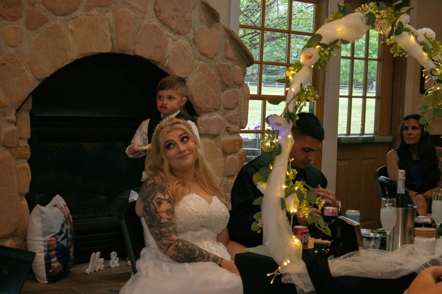 Wedding celebration by stone fireplace with decorative floral arch.