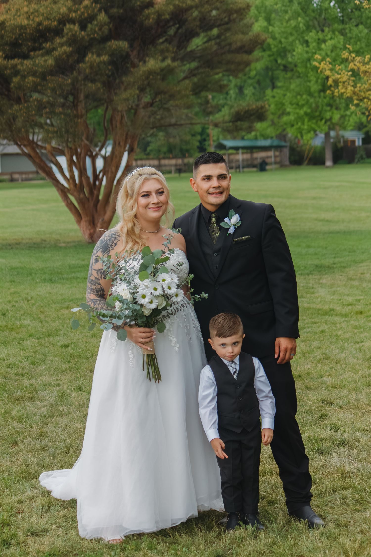 Wedding party poses together outdoors with greenery and trees in background.