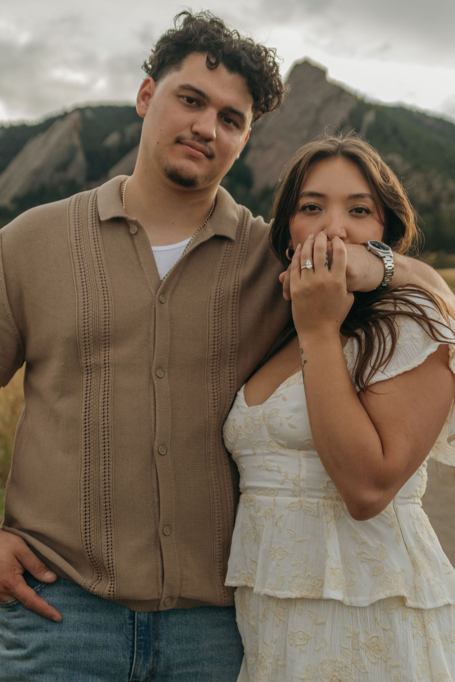 Engaged couple poses together in front of dramatic Flatirons mountains, woman showing off engagement ring.