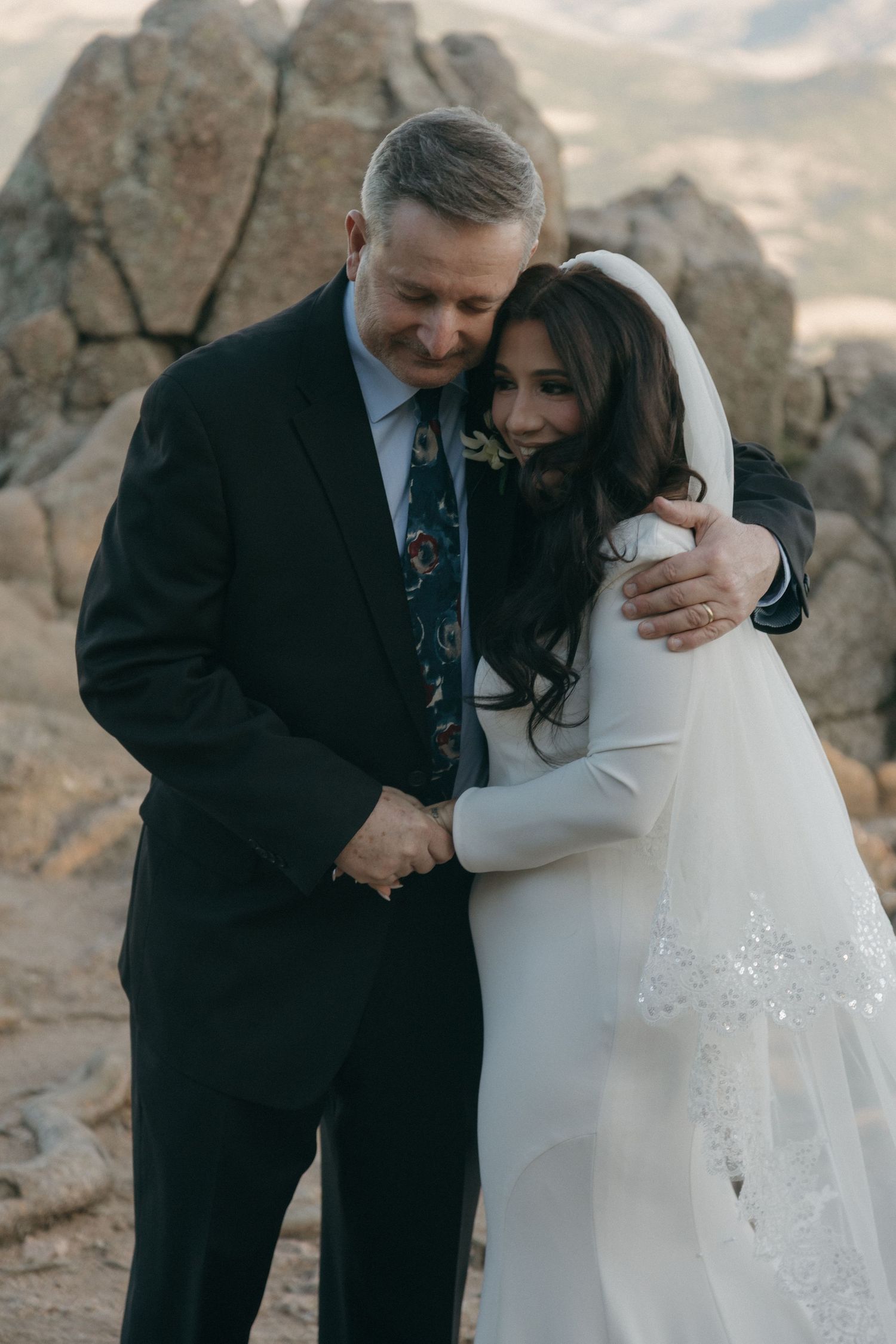Bride and groom share a tender embrace on a rocky mountain landscape during their elopement.