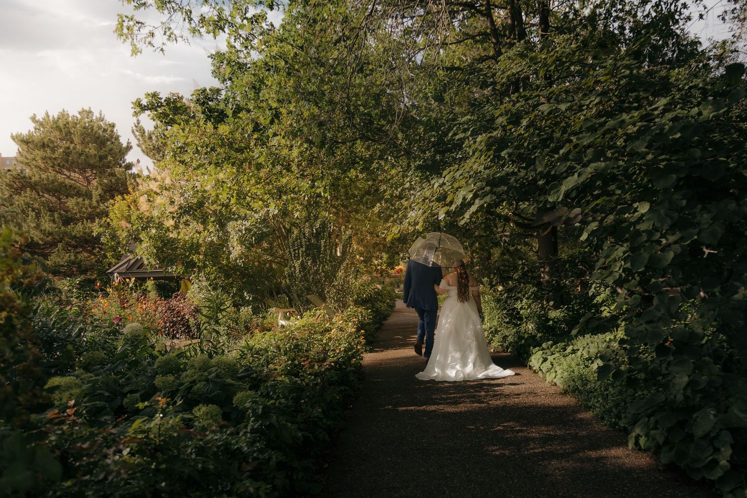 Bride and groom walking hand-in-hand through a lush garden archway on their wedding day.