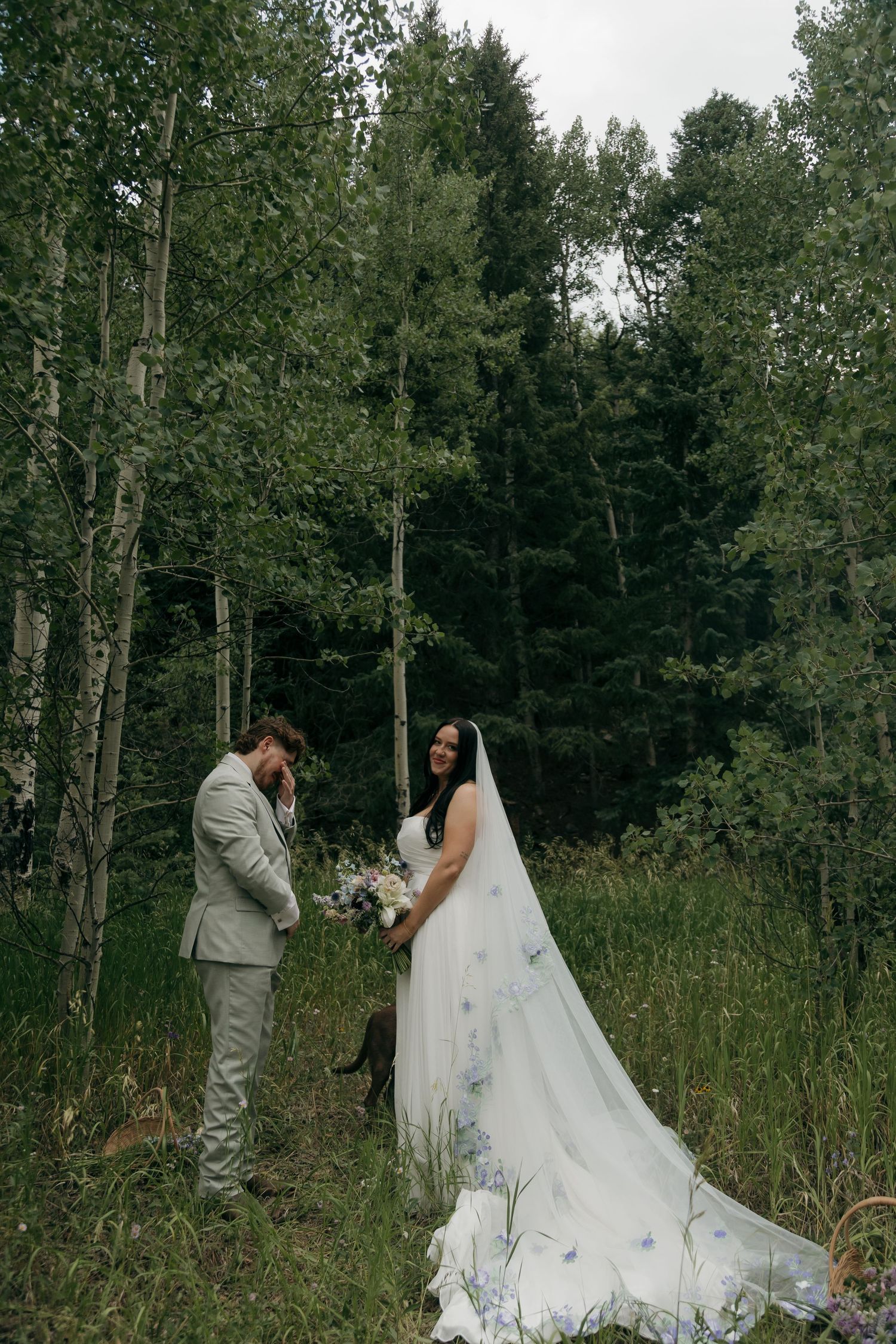 Bride and groom share an emotional first look moment in a forest, bride holding wildflower bouquet with floral veil.