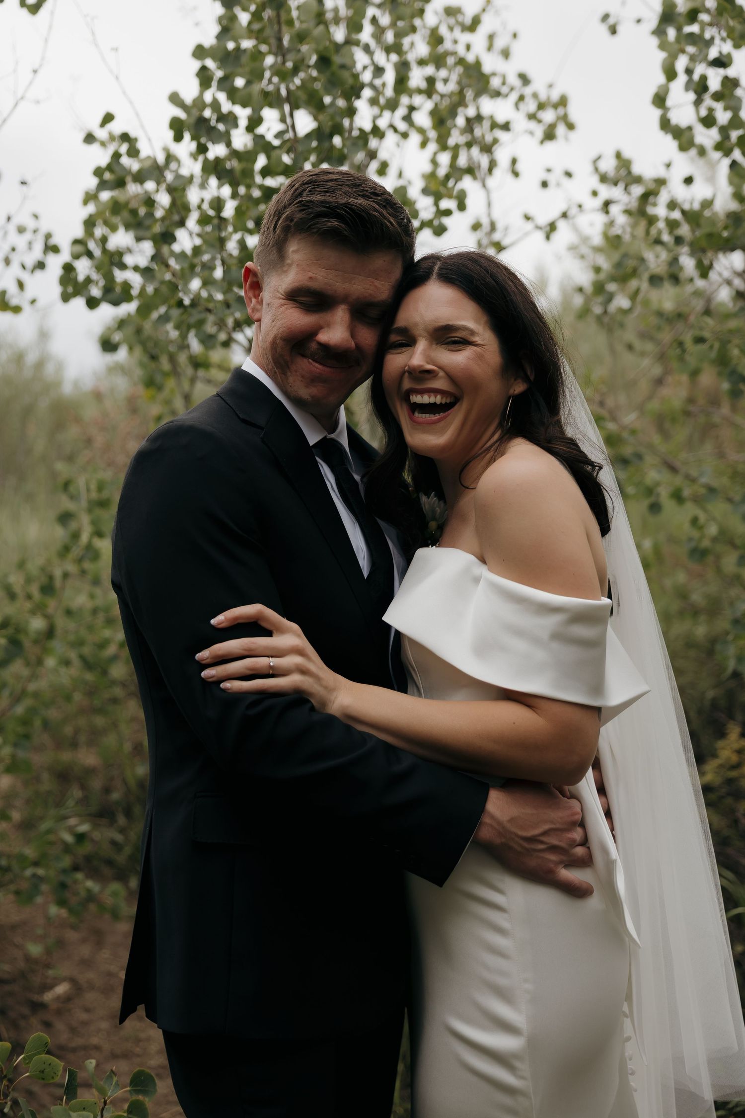 Joyful bride and groom laughing together outdoors surrounded by autumn trees.