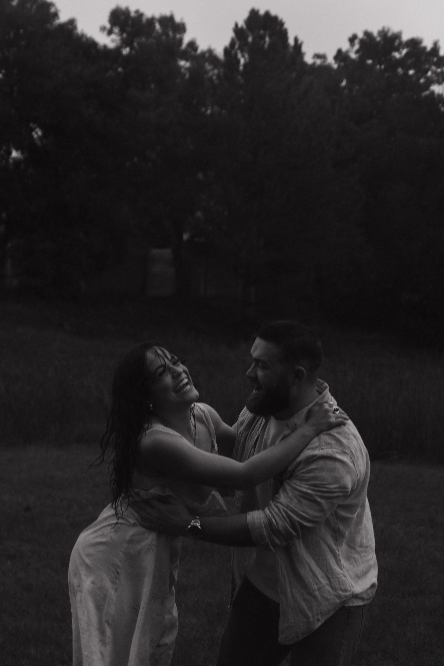 Couple embraces intimately in a darkening field at twilight.