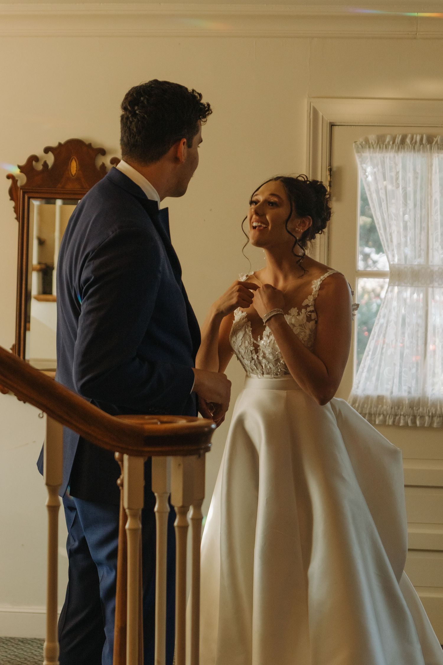 A couple in wedding attire sharing an emotional first look moment in a sunlit room.