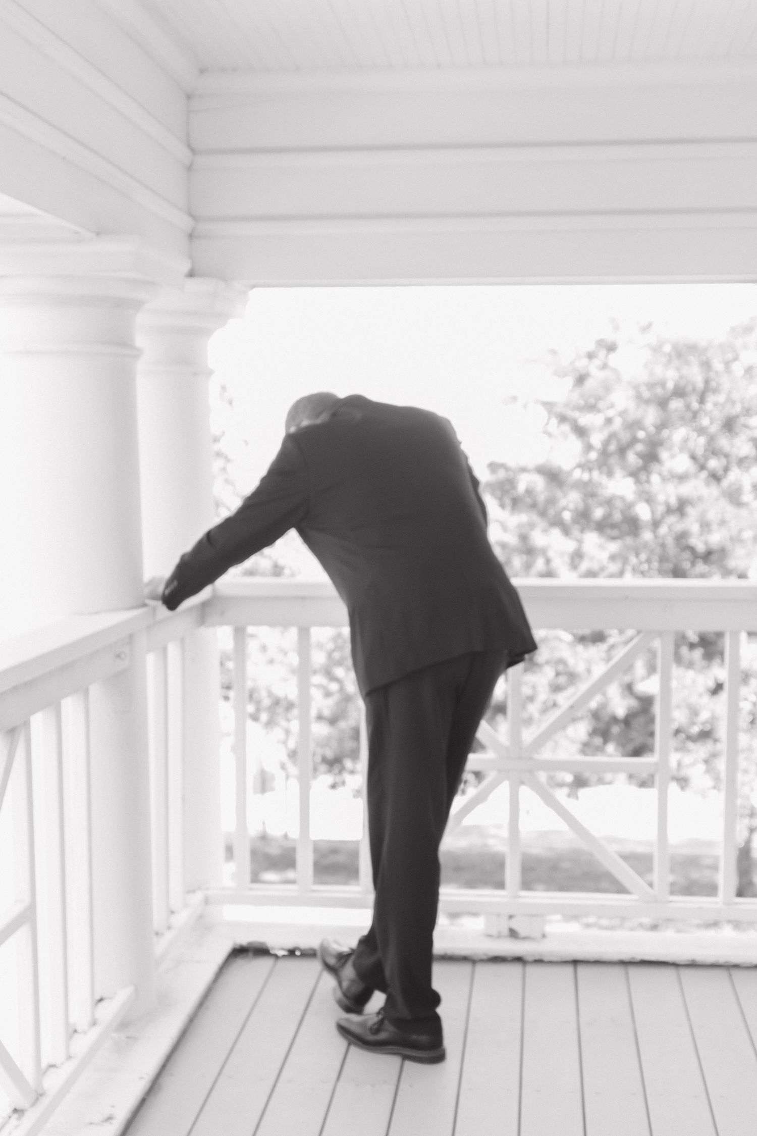 Person in formal attire leans dramatically on a white porch railing.
