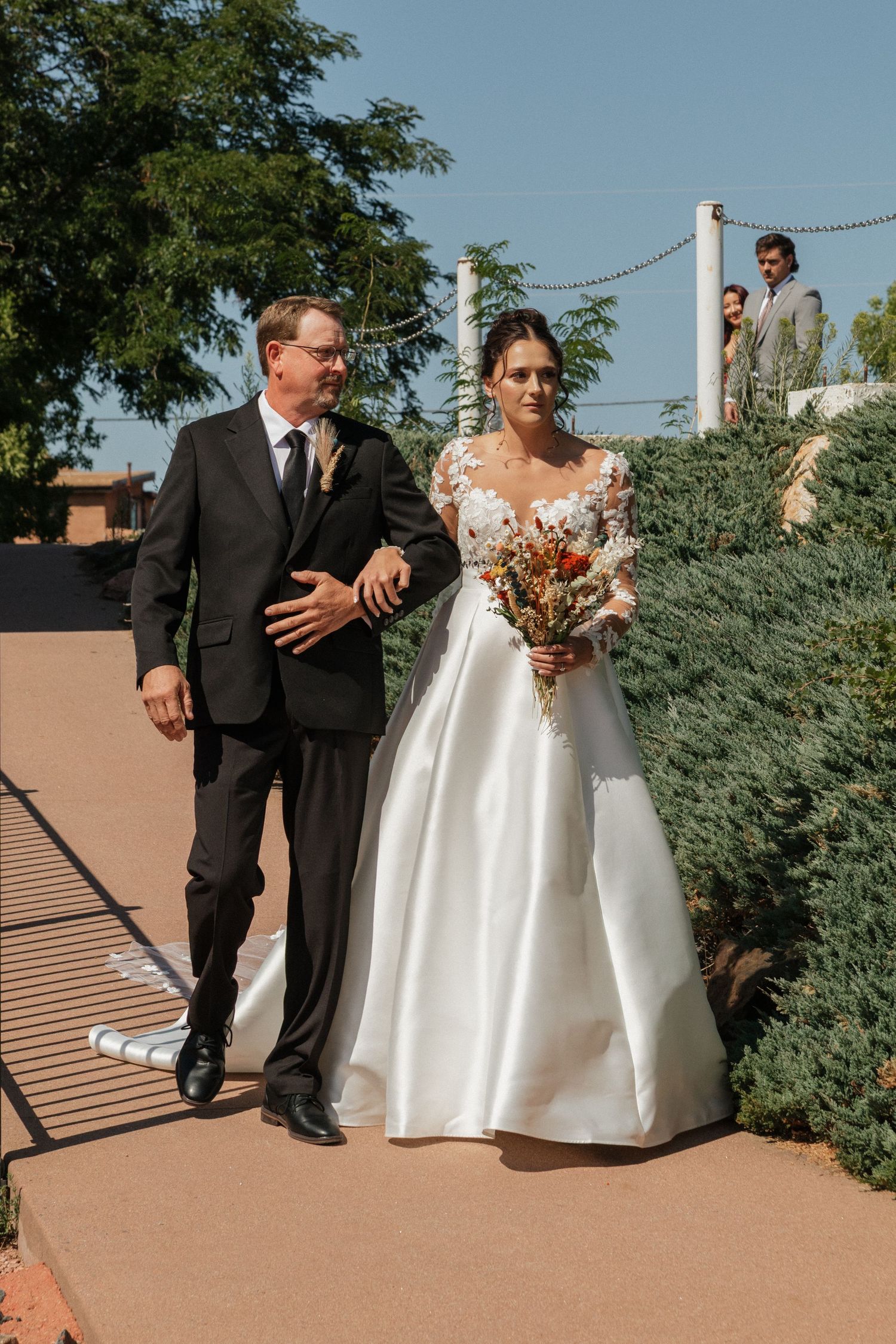 Wedding party walking along outdoor pathway with mountains and greenery in background.
