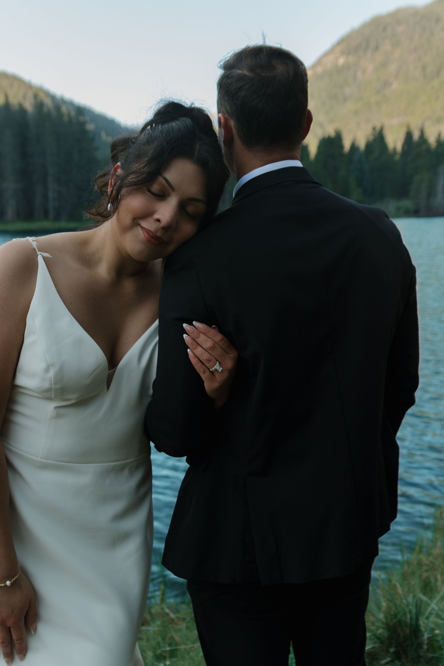 A romantic moment between newlyweds by a mountain lake during sunset.