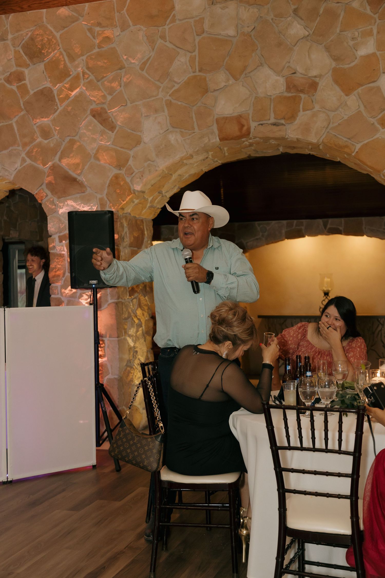 Man in cowboy hat gives a speech with microphone at wedding reception.