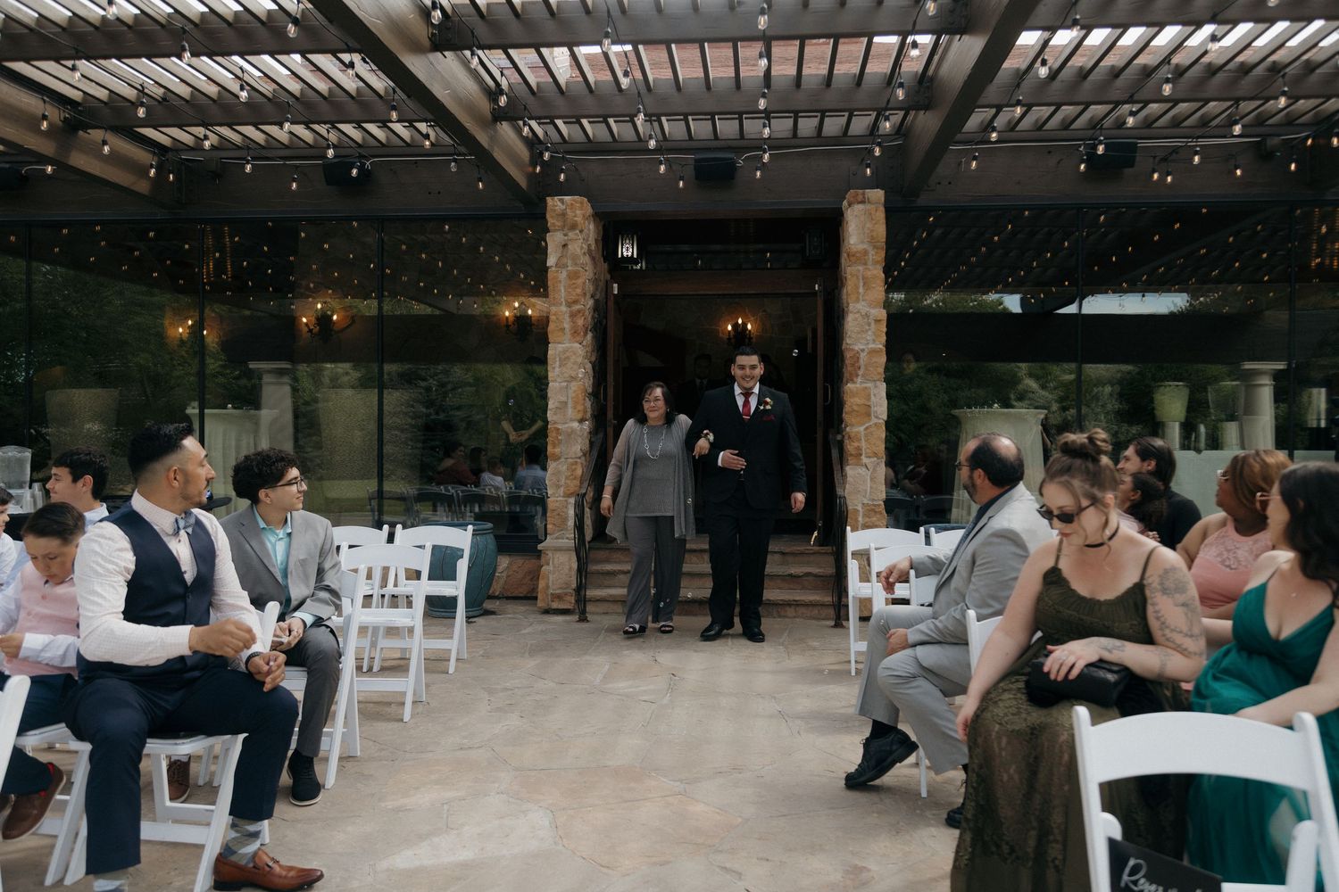 Wedding ceremony processional with guests seated in white chairs at an elegant outdoor venue.