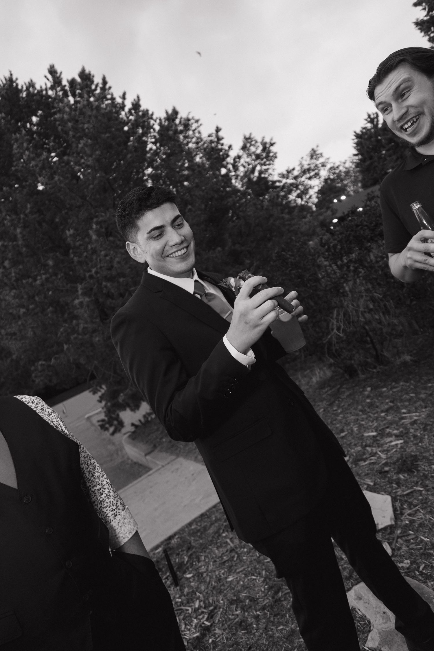 Black and white photo of smiling groomsmen celebrating outdoors at wedding reception.