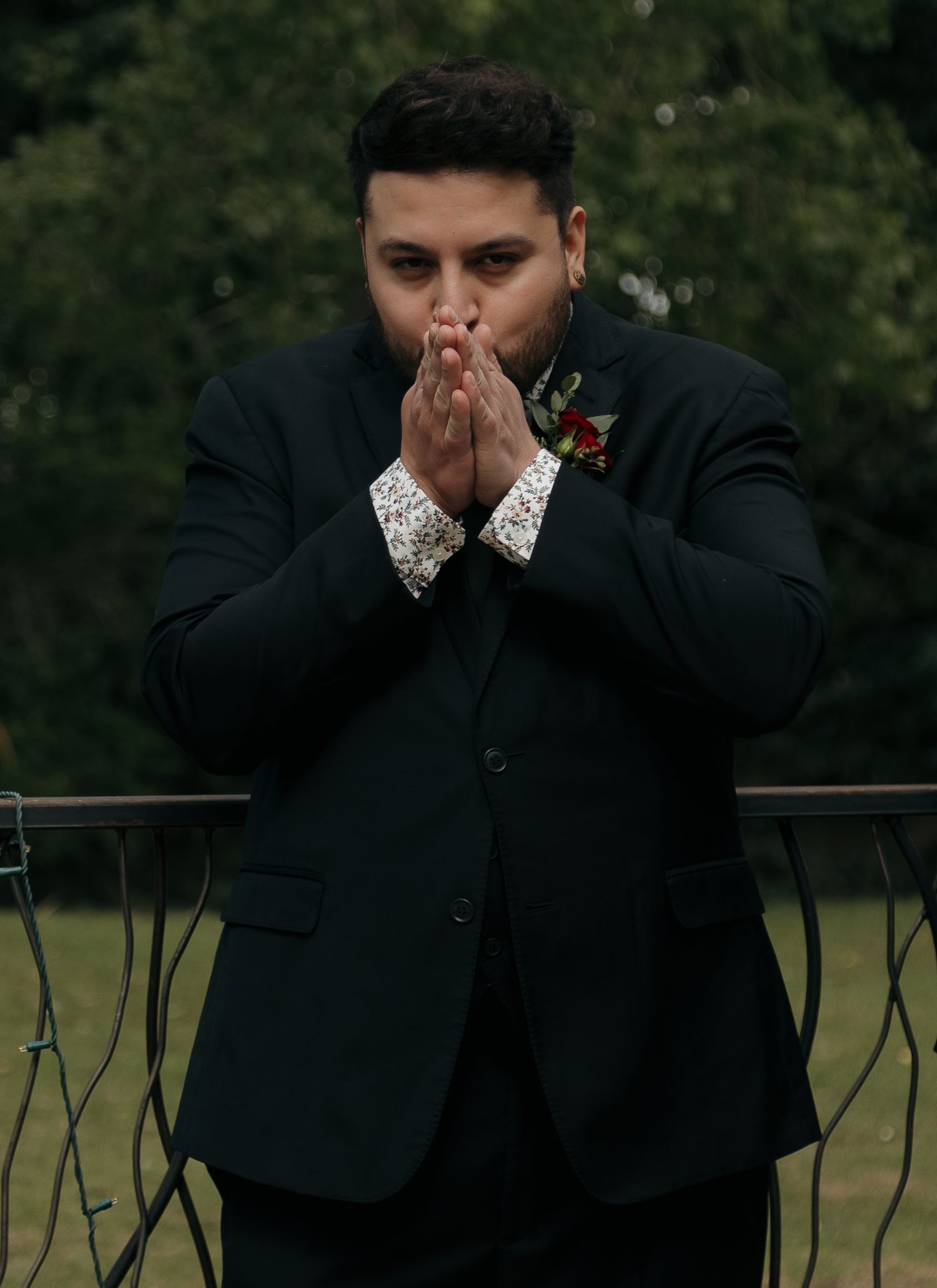 Emotional man in dark suit with floral boutonniere holds hands together in prayer at a wedding.