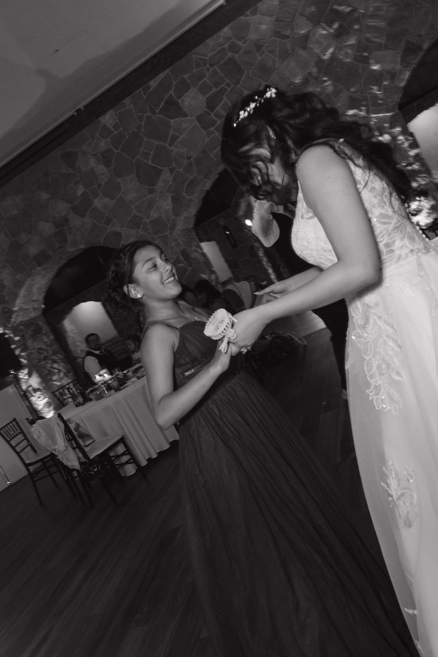 Black and white photo of bride dancing joyfully with a young girl in a ballgown at the wedding reception.