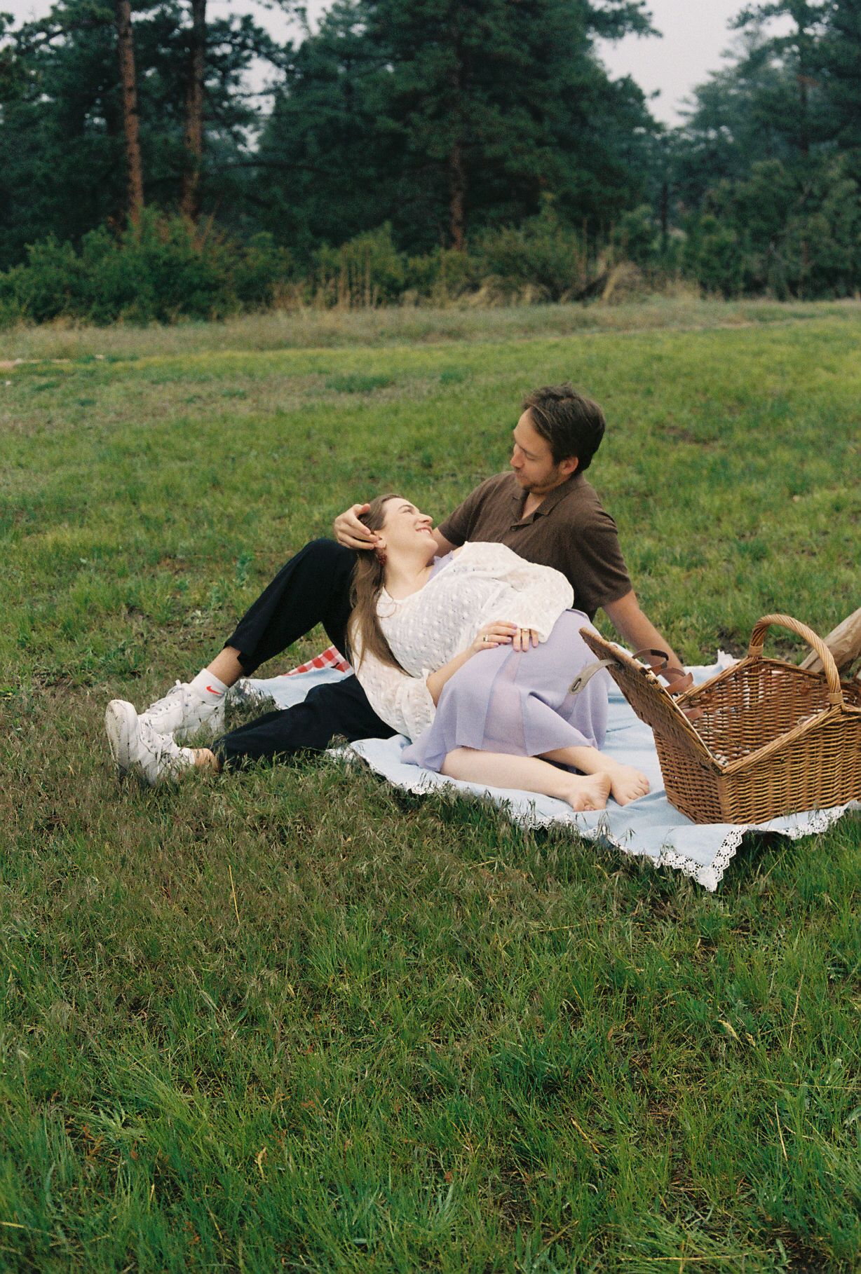Couple relaxing on a picnic blanket in a green field, woman laughing while lying across mans lap.