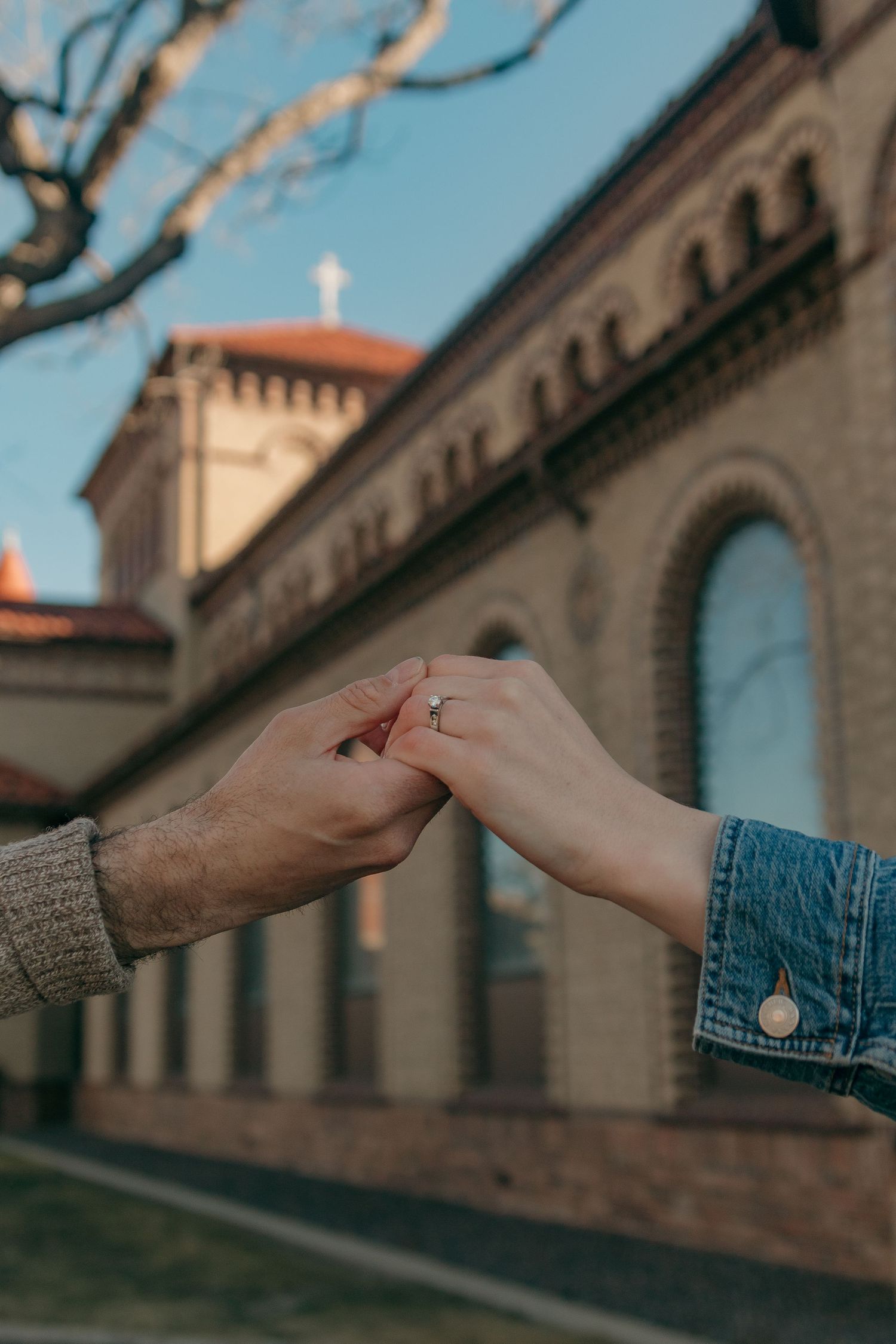 Two hands reaching out to touch each other against a backdrop of historic stone architecture with arched windows.