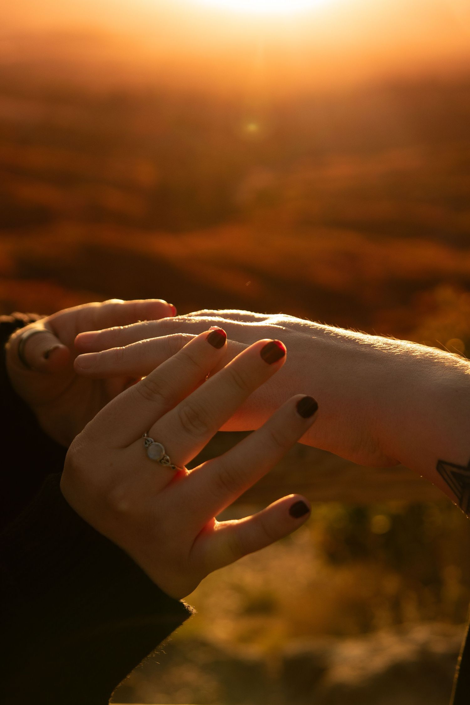 Hand holding a cigarette against a warm orange sunset sky with dramatic lighting and silhouetted background.