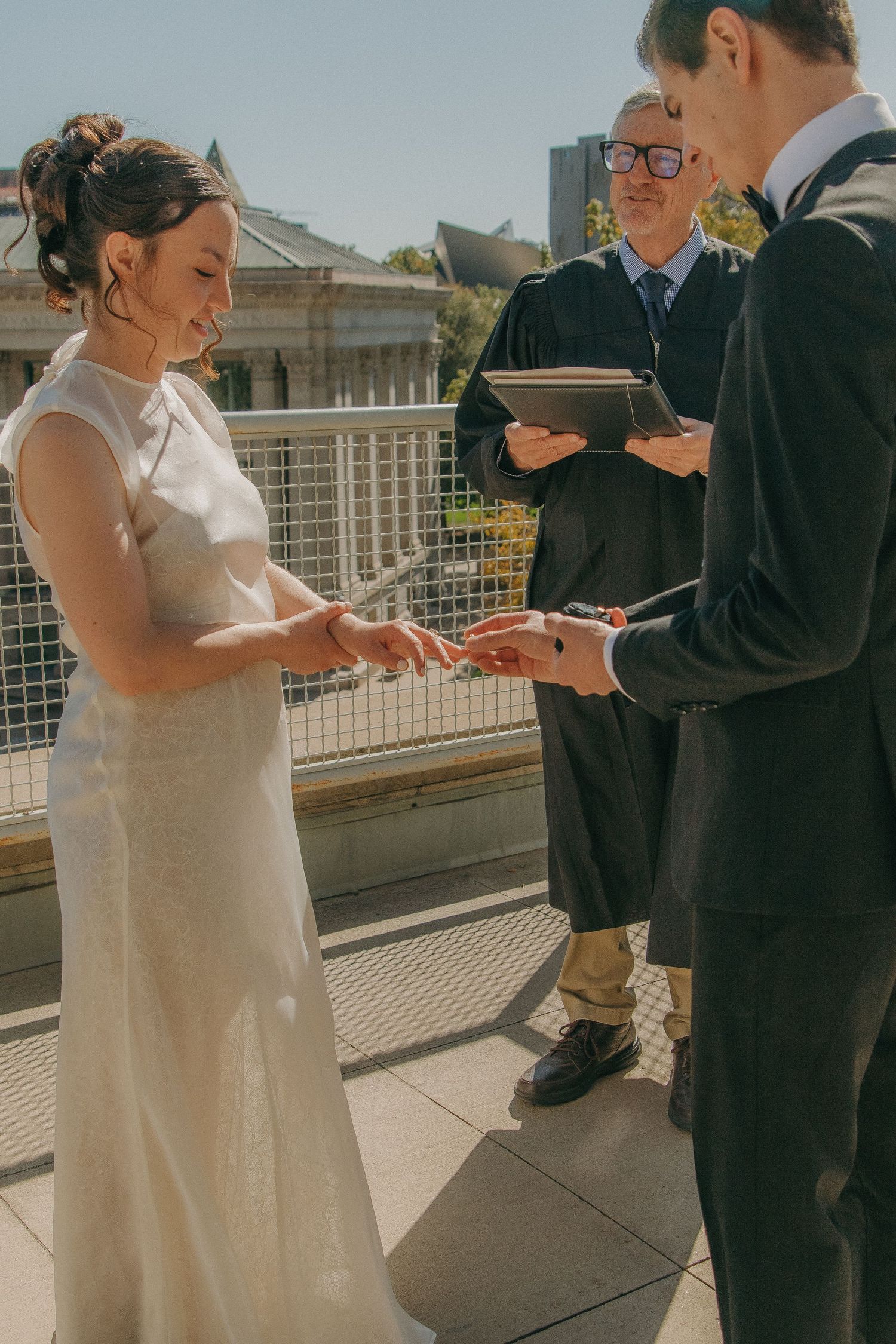 Couple exchanging rings during outdoor wedding ceremony on sunny terrace.