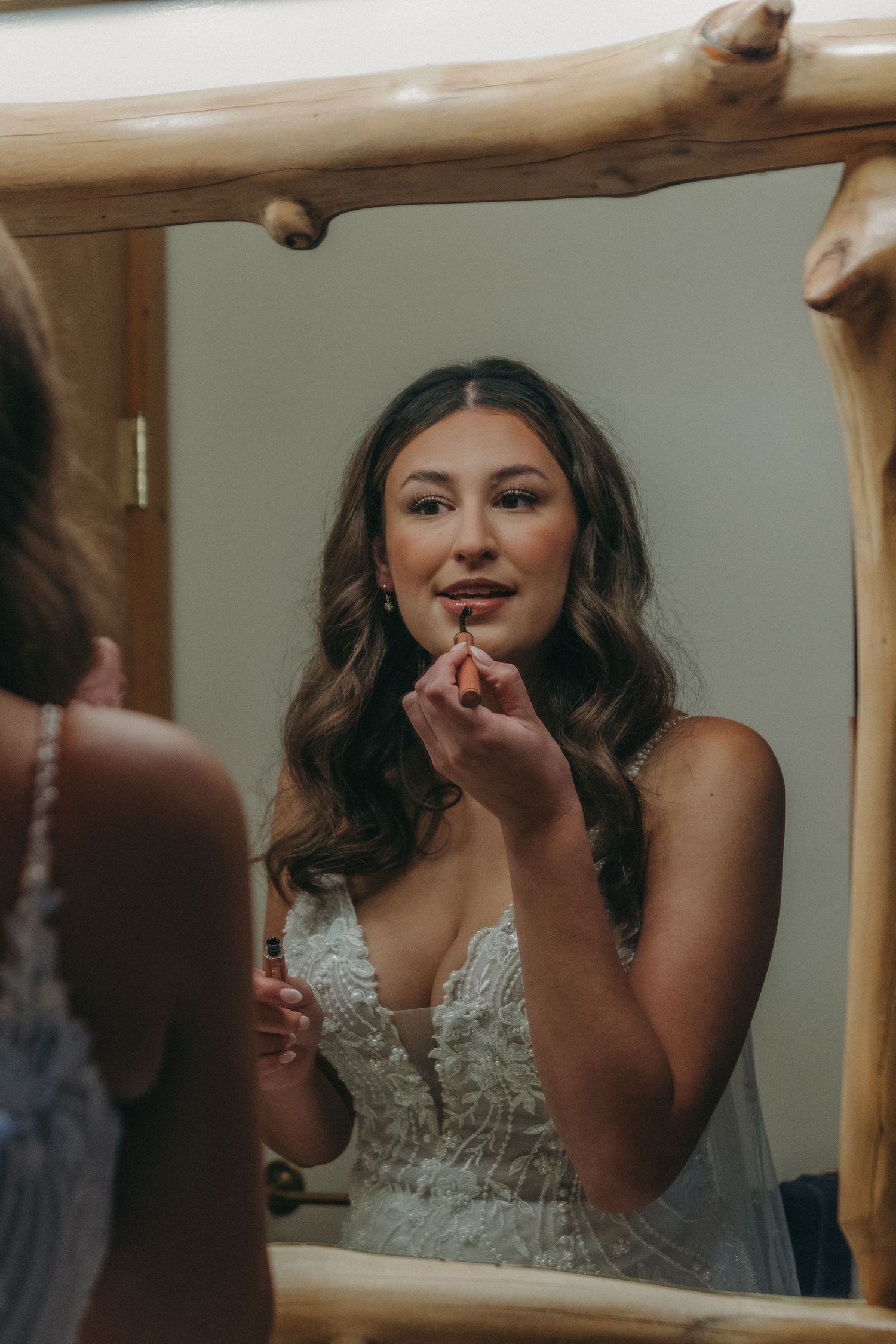 Bride applying makeup in a mirror with natural lighting.