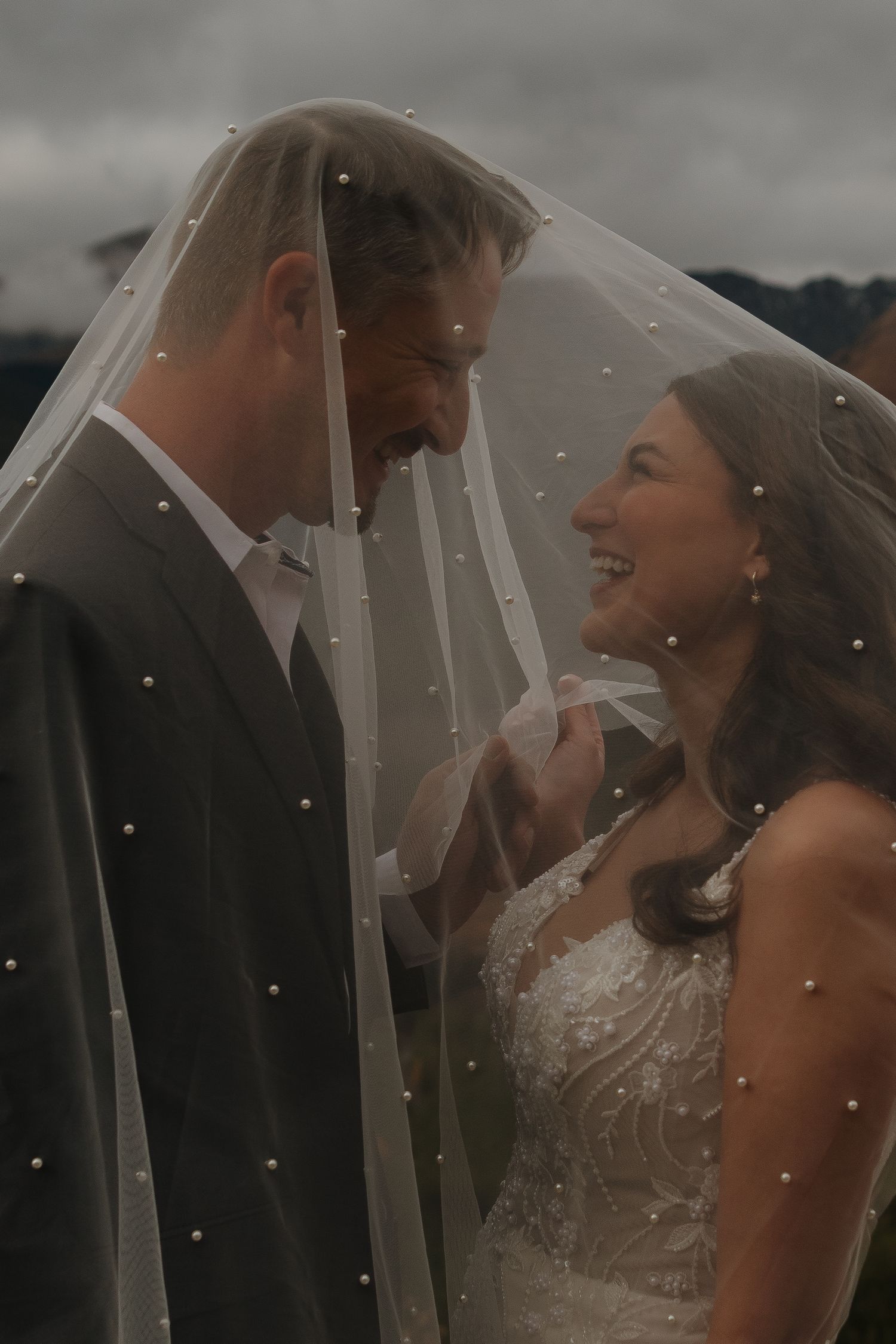 A romantic moment under a wedding veil with raindrops in the mountain air.
