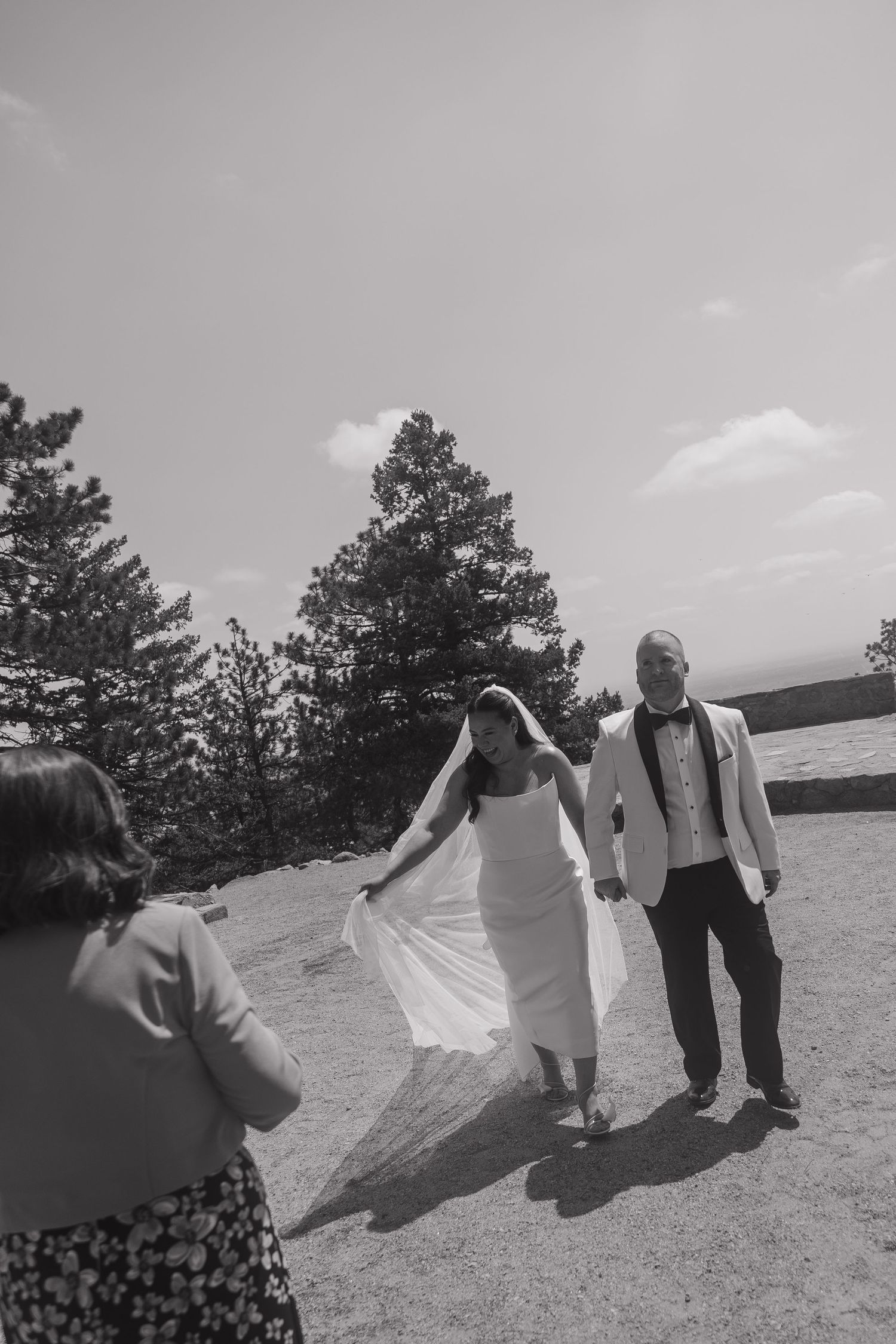 Bride and groom walk hand in hand on rocky mountain overlook in black and white.