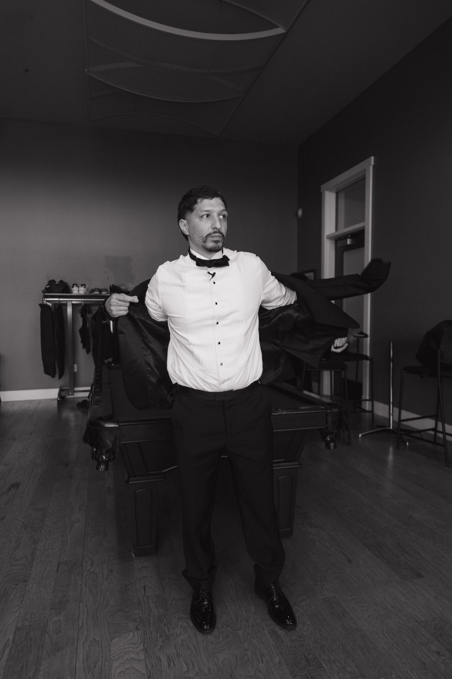 Groom in white dress shirt puts on suit jacket in black and white getting-ready wedding photo.