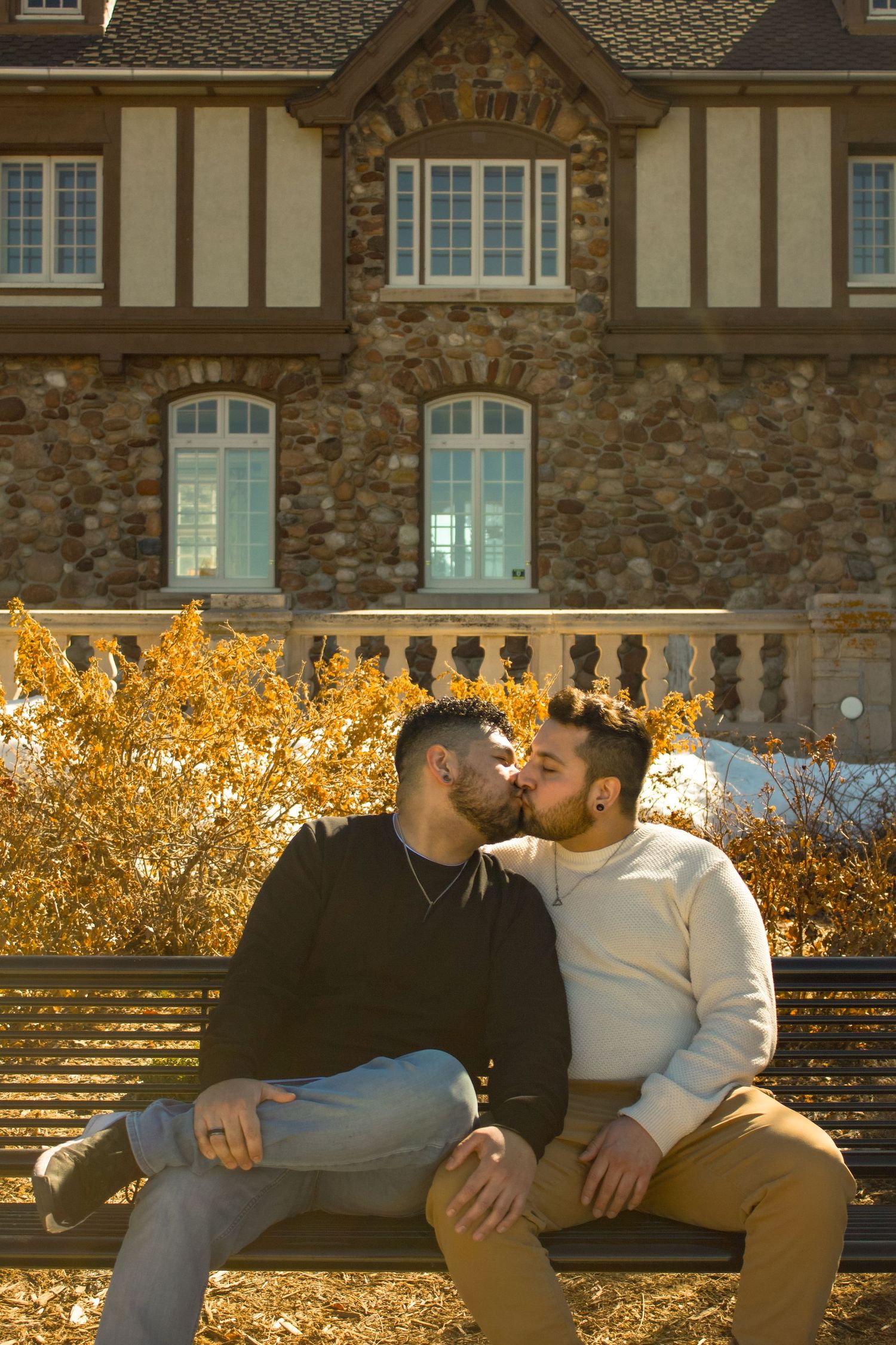 Two people share a tender moment on a bench against the backdrop of a grand stone building.