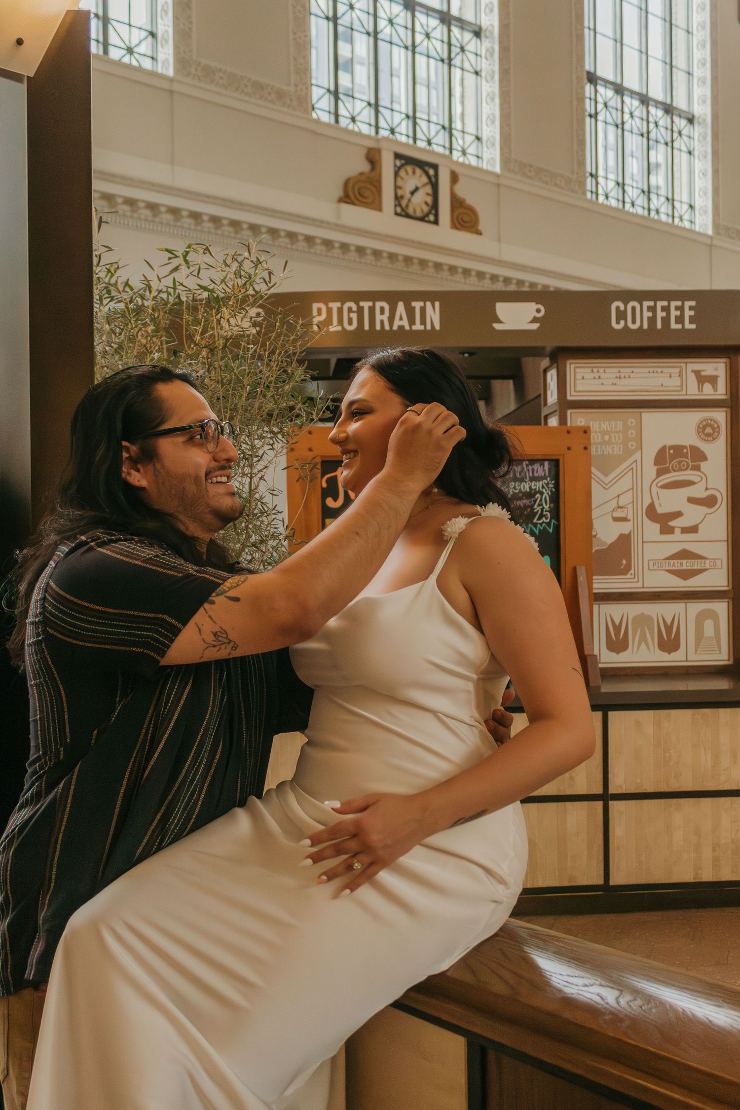 A playful couple poses in front of a coffee shop sign indoors.
