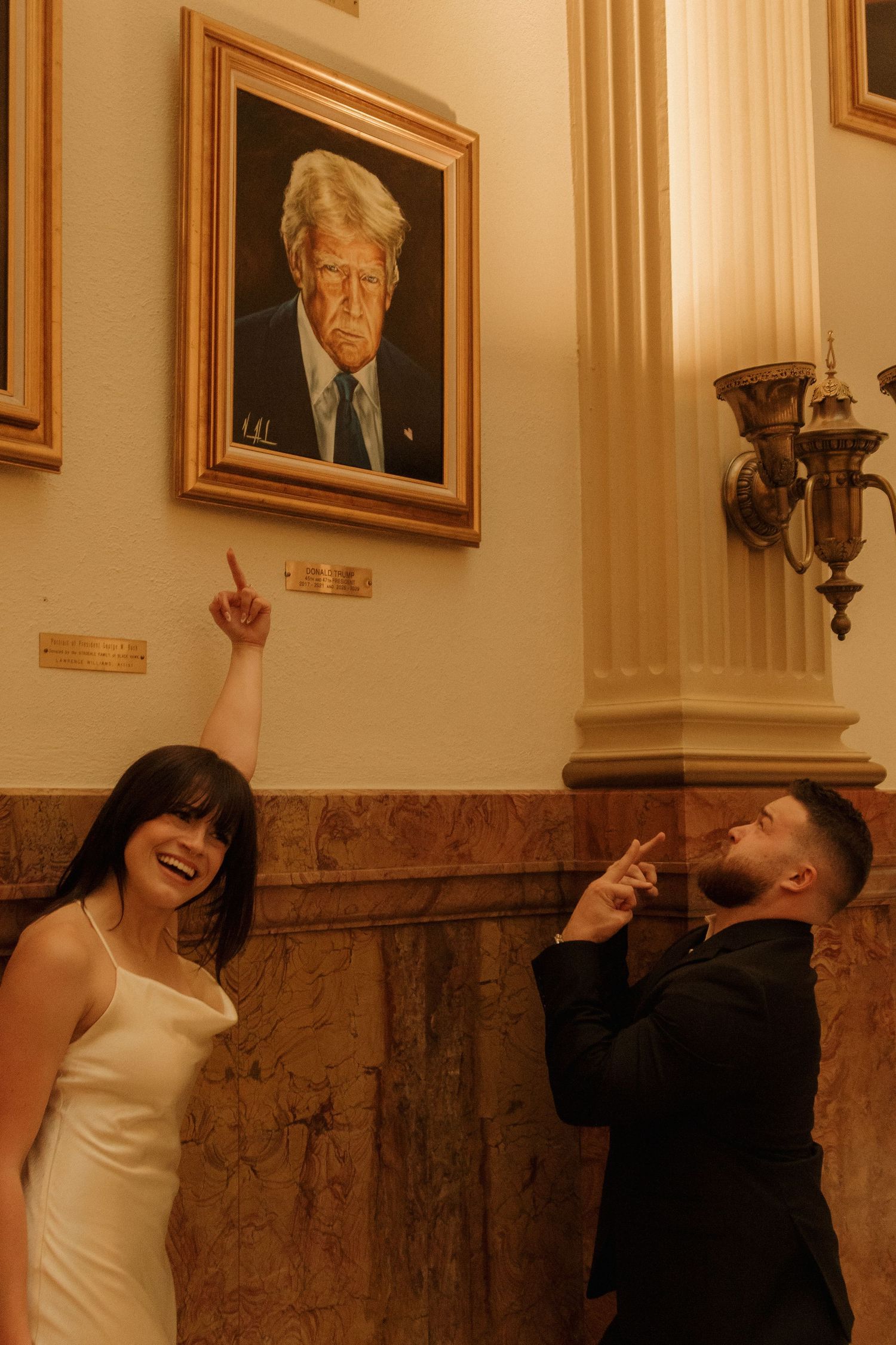 Playful couple posing beneath a portrait in an elegant hallway.