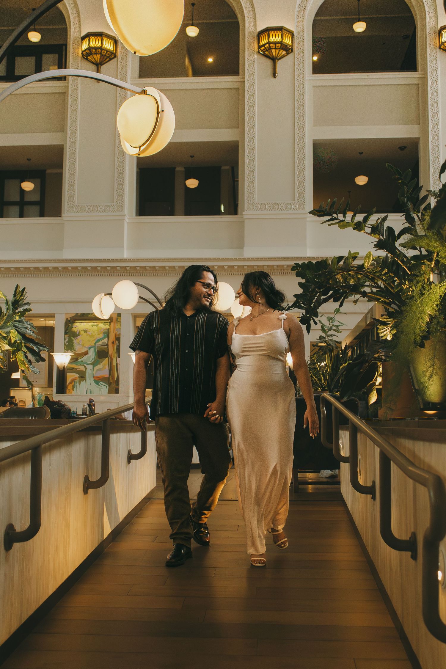 People walking through an elegant hallway with arched ceilings and hanging pendant lights.