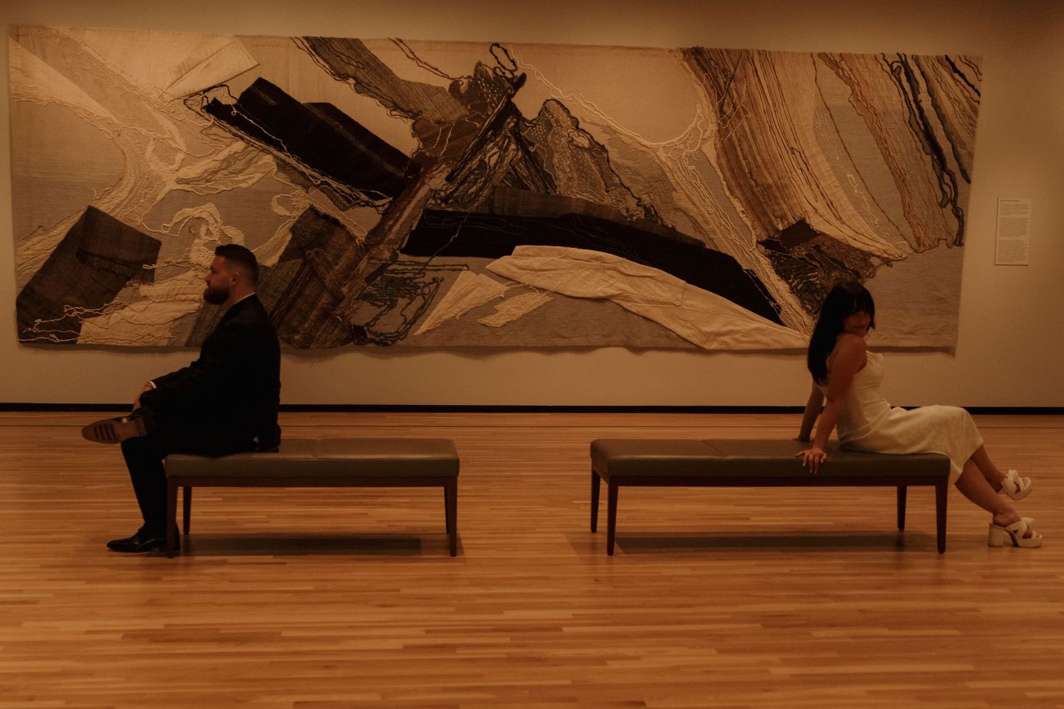 Dramatic sepia-toned photographs displayed in sequence show figures in an art gallery space.