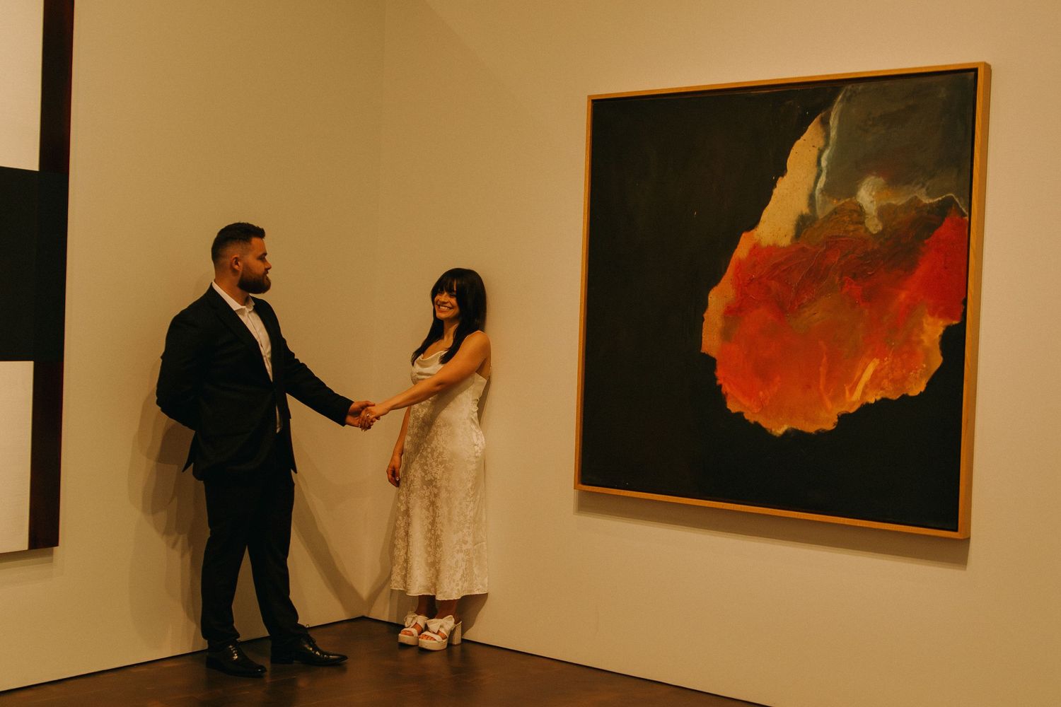 Two people dance gracefully in an art gallery with modern paintings displayed on white walls.