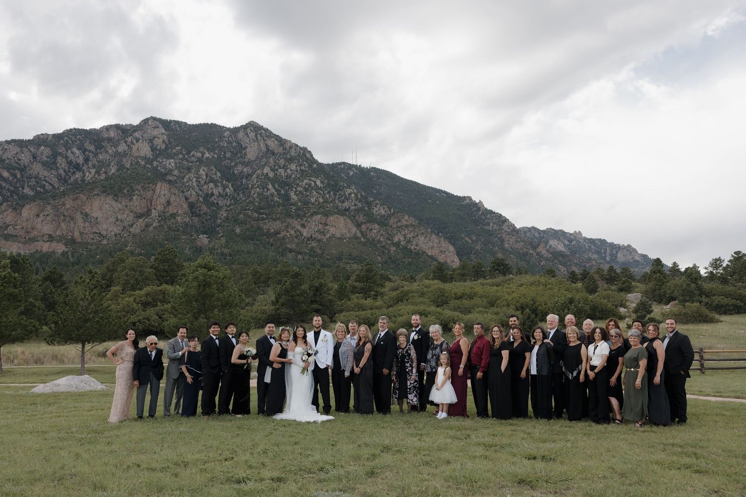 Wedding party poses in a green meadow with stunning Rocky Mountain backdrop under cloudy skies in Colorado.