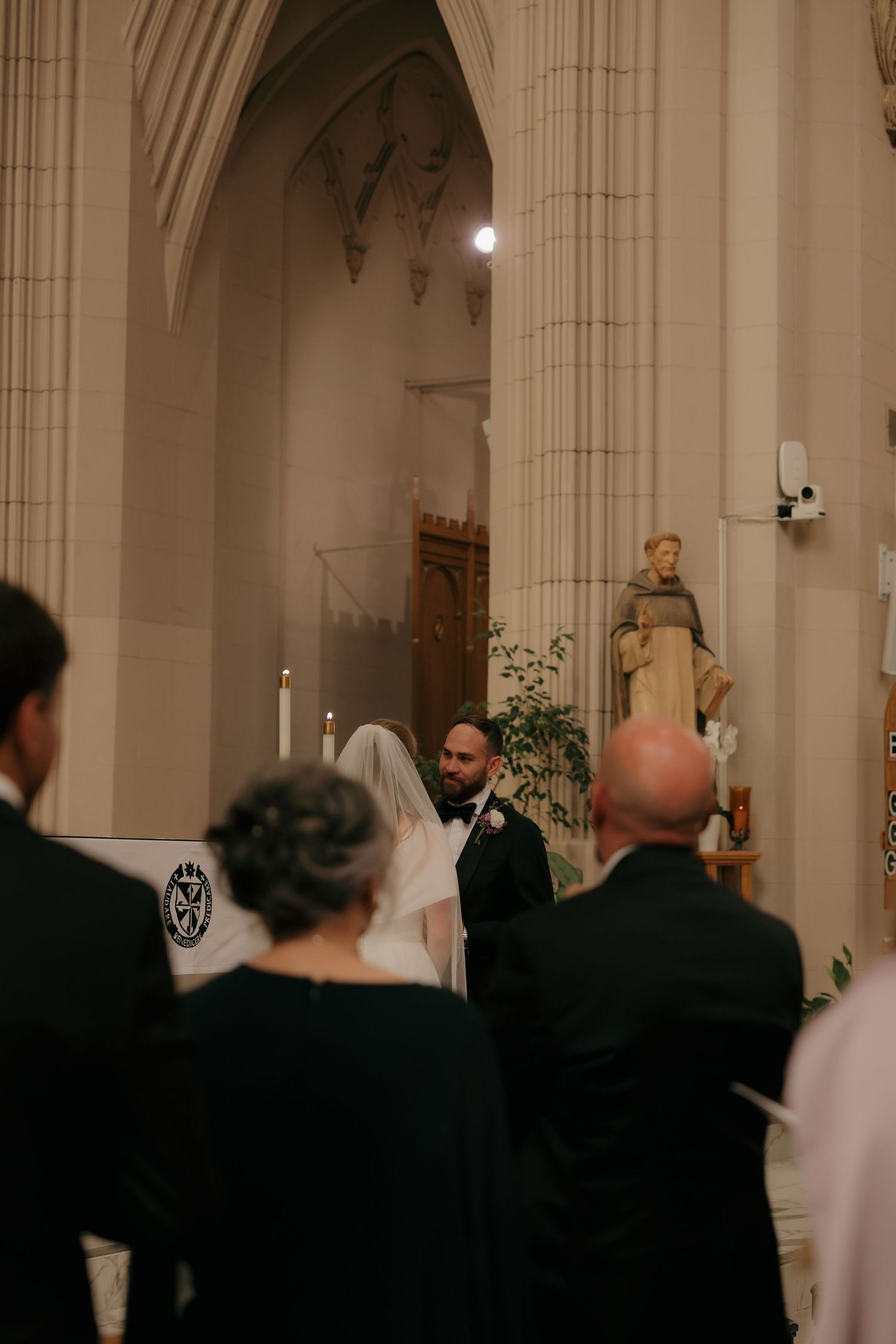 Wedding ceremony inside a grand cathedral with gothic arches and a statue of a saint.