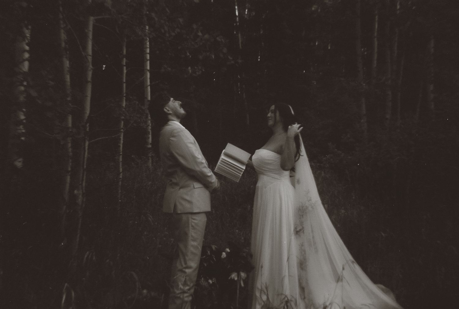 Vintage black and white photo of bride and groom reading vows in a birch forest during their elopement.