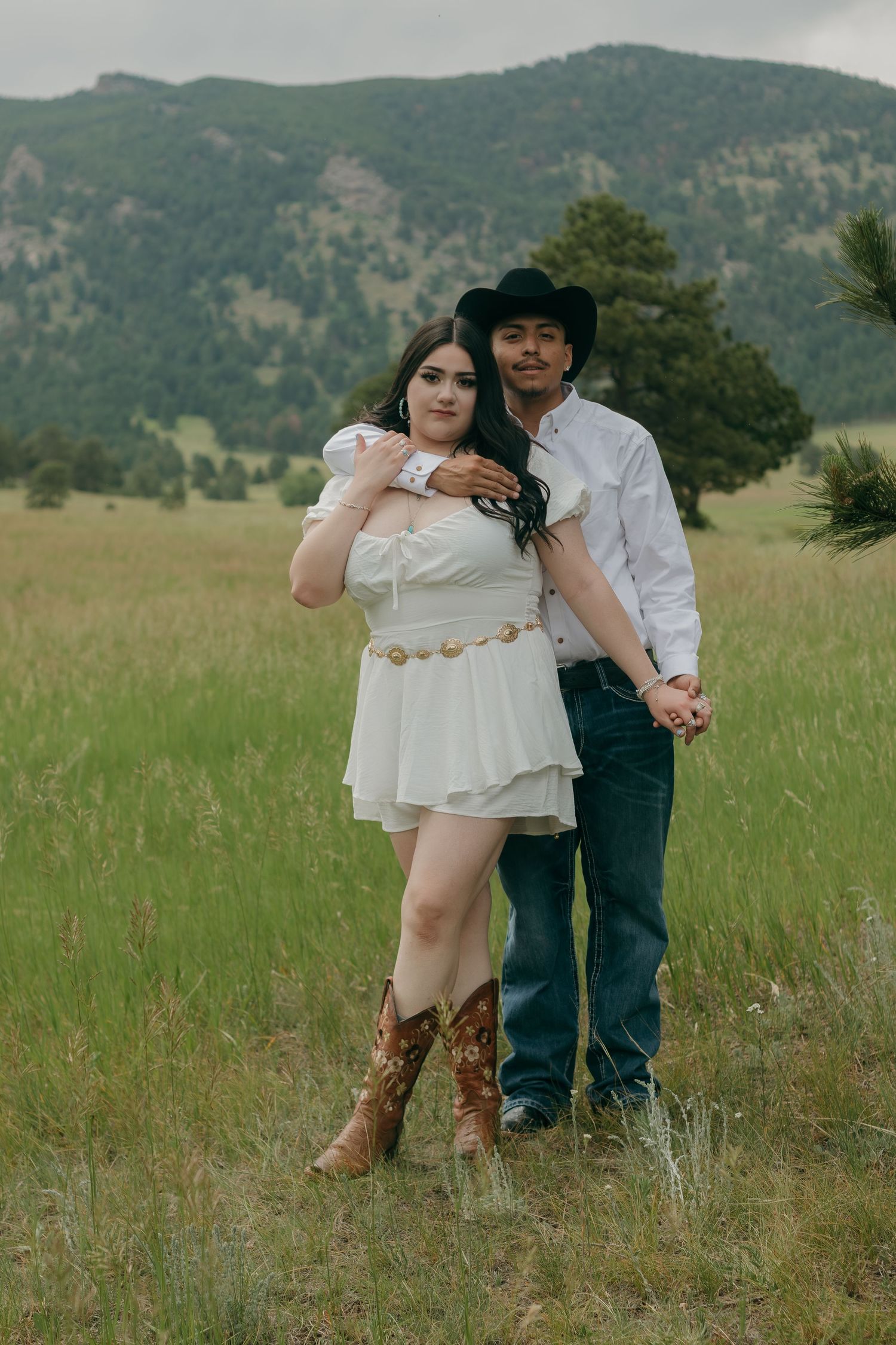 A tender moment captured in a mountain meadow with someone wearing cowboy boots and a white dress.