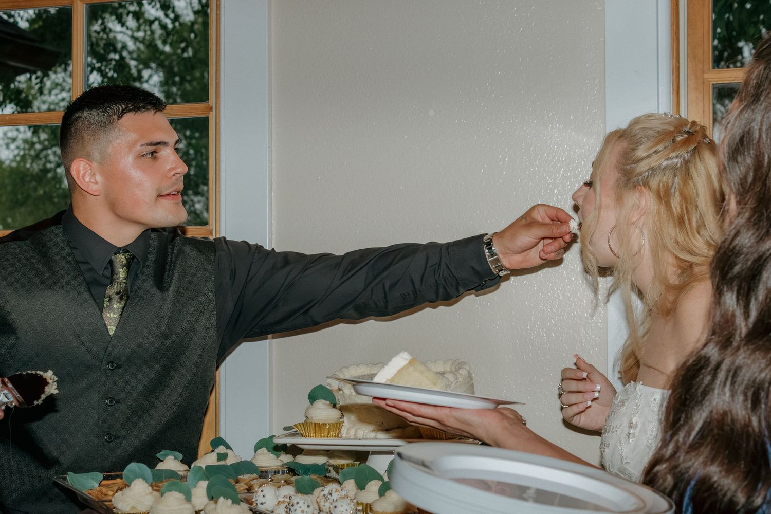 Wedding cake feeding moment at reception with dessert display in foreground.
