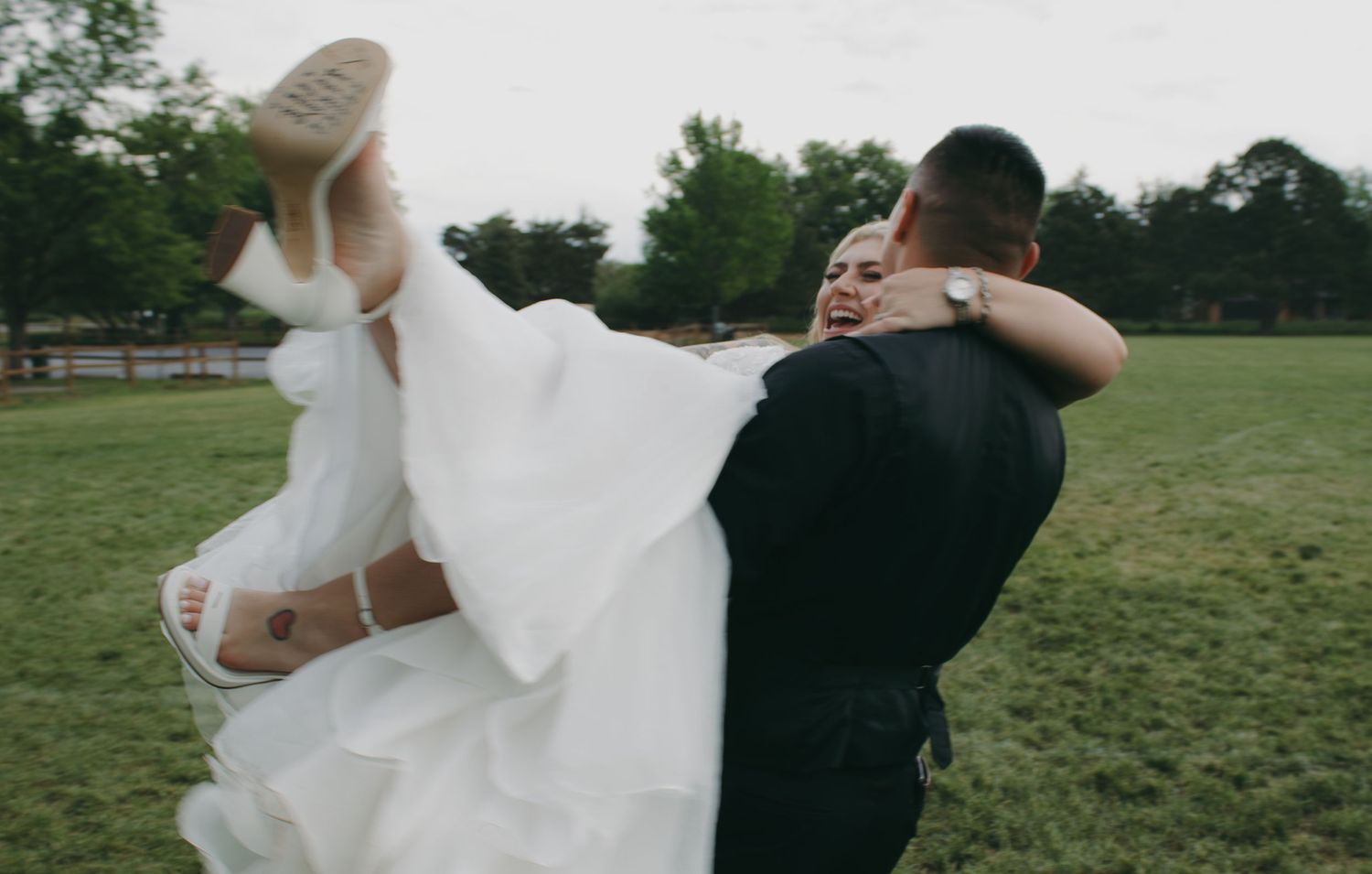 Wedding couple spins together in a grassy meadow creating a flowing motion with the bride's dress.