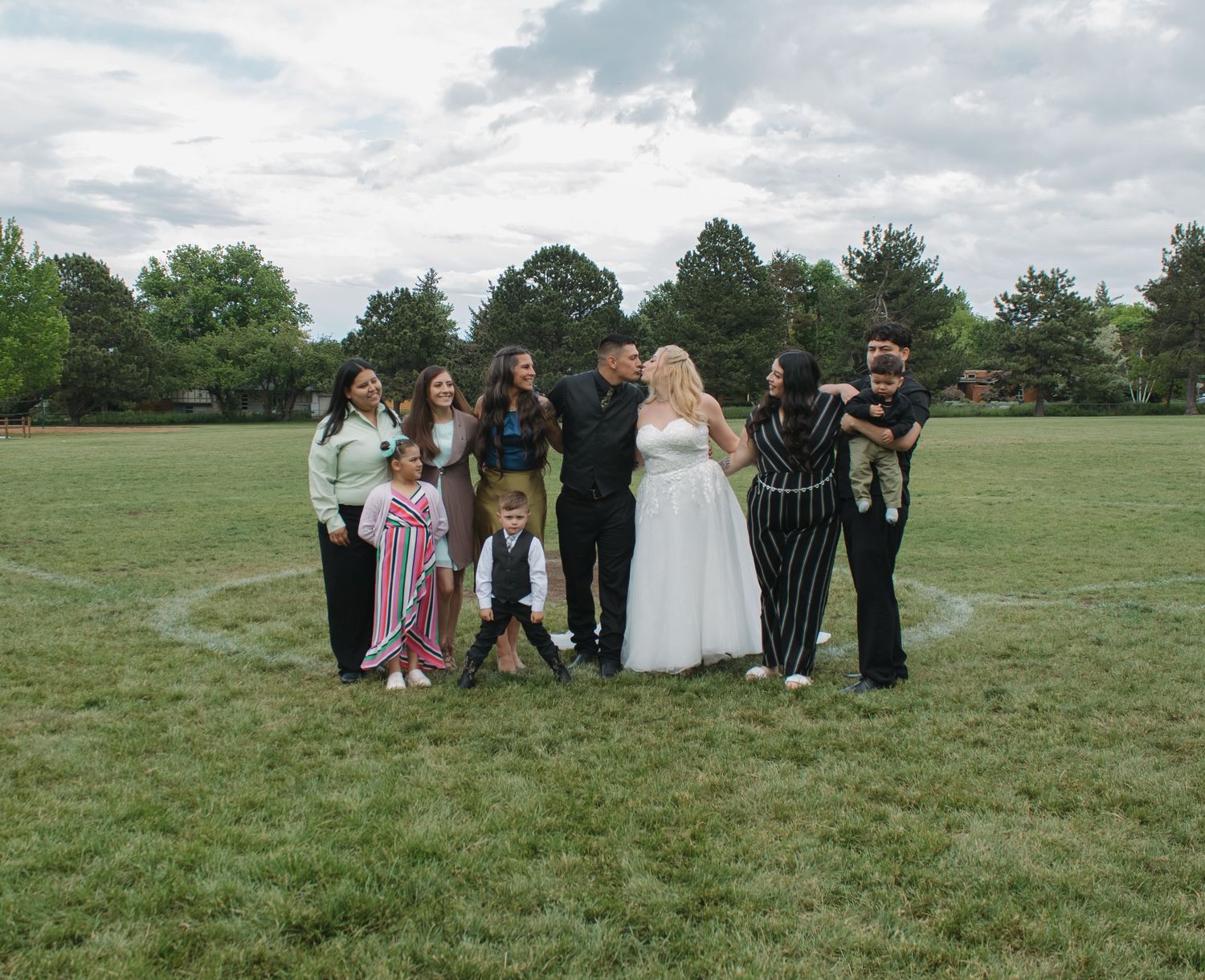 Wedding party lined up for group photos on green grass field.