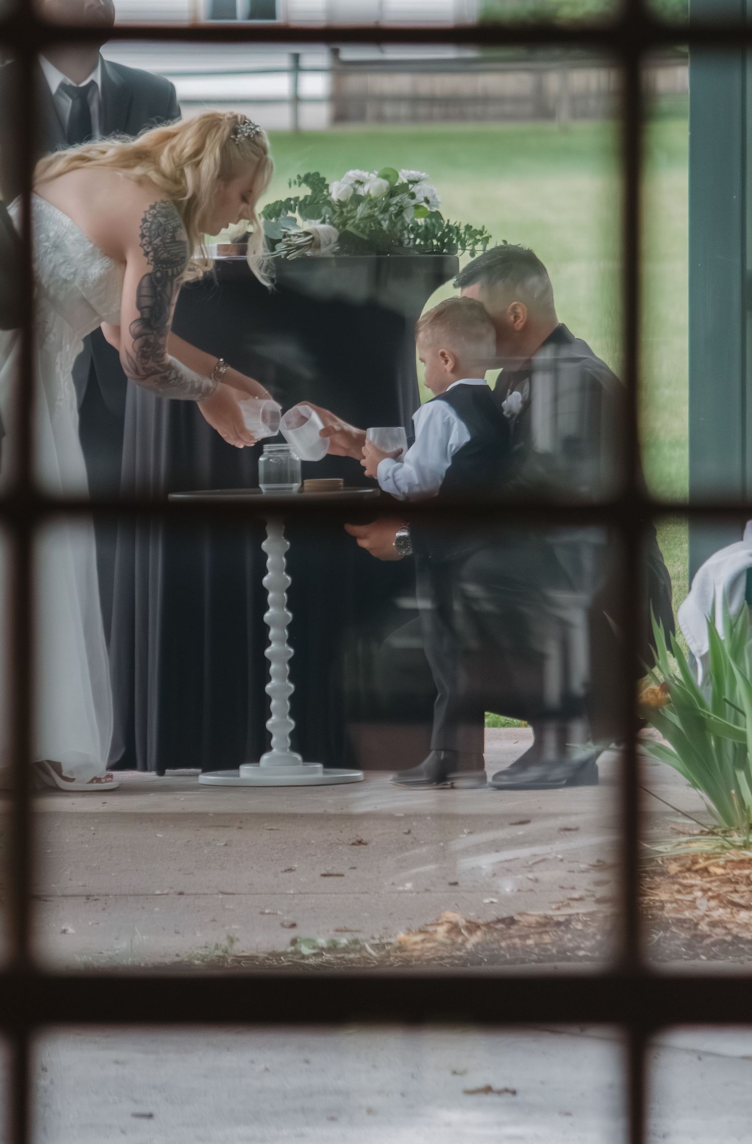 Through window panes, a child participates in what appears to be a wedding ceremony.