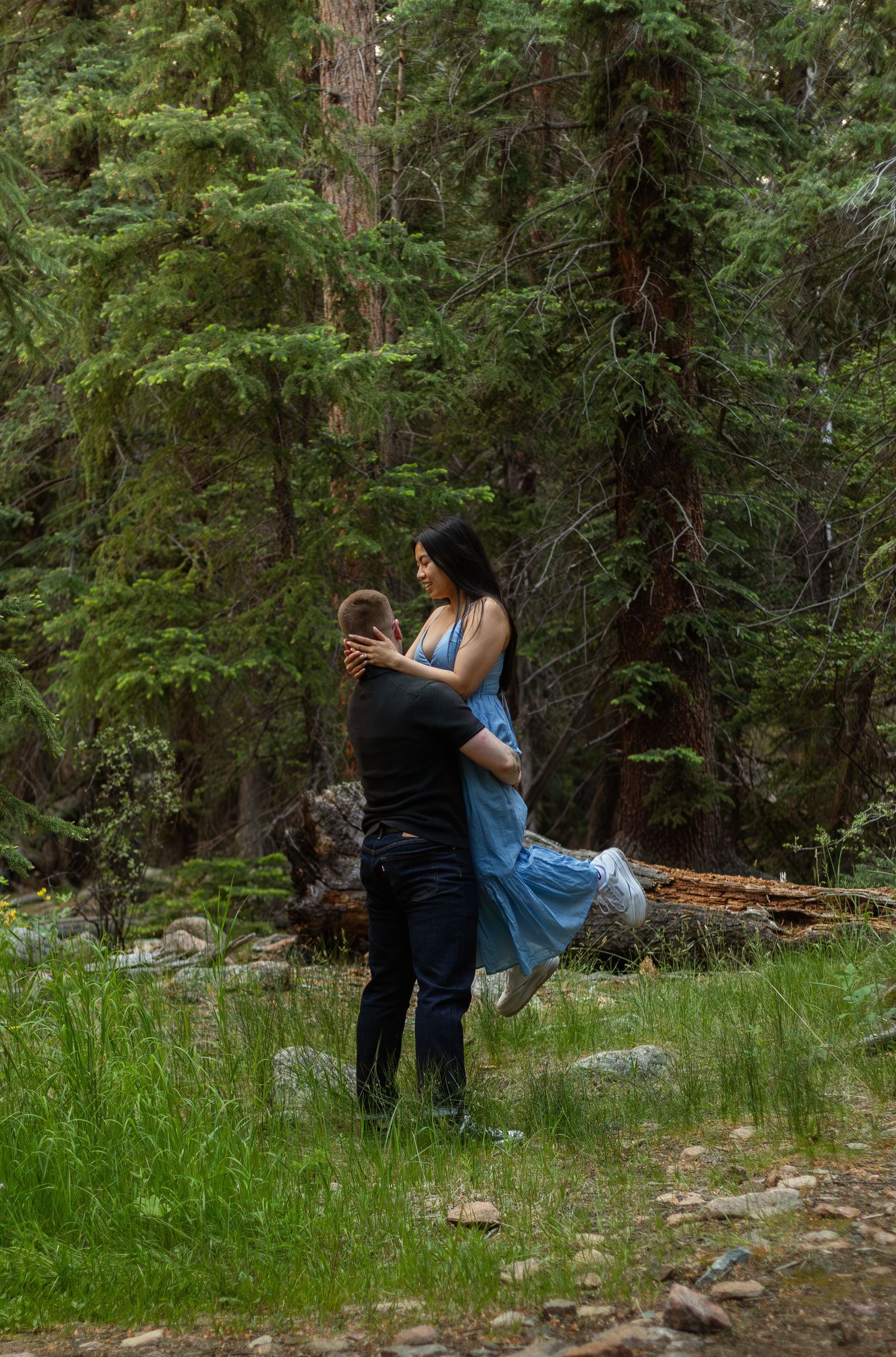 A couple shares a romantic dance pose surrounded by tall evergreen trees in a forest clearing.