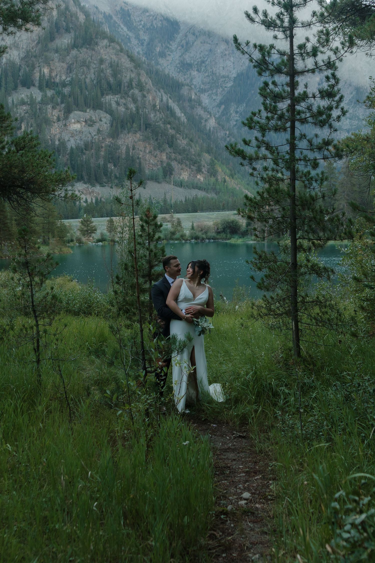 Wedding couple walking along mountain trail with scenic lake and mountain views.