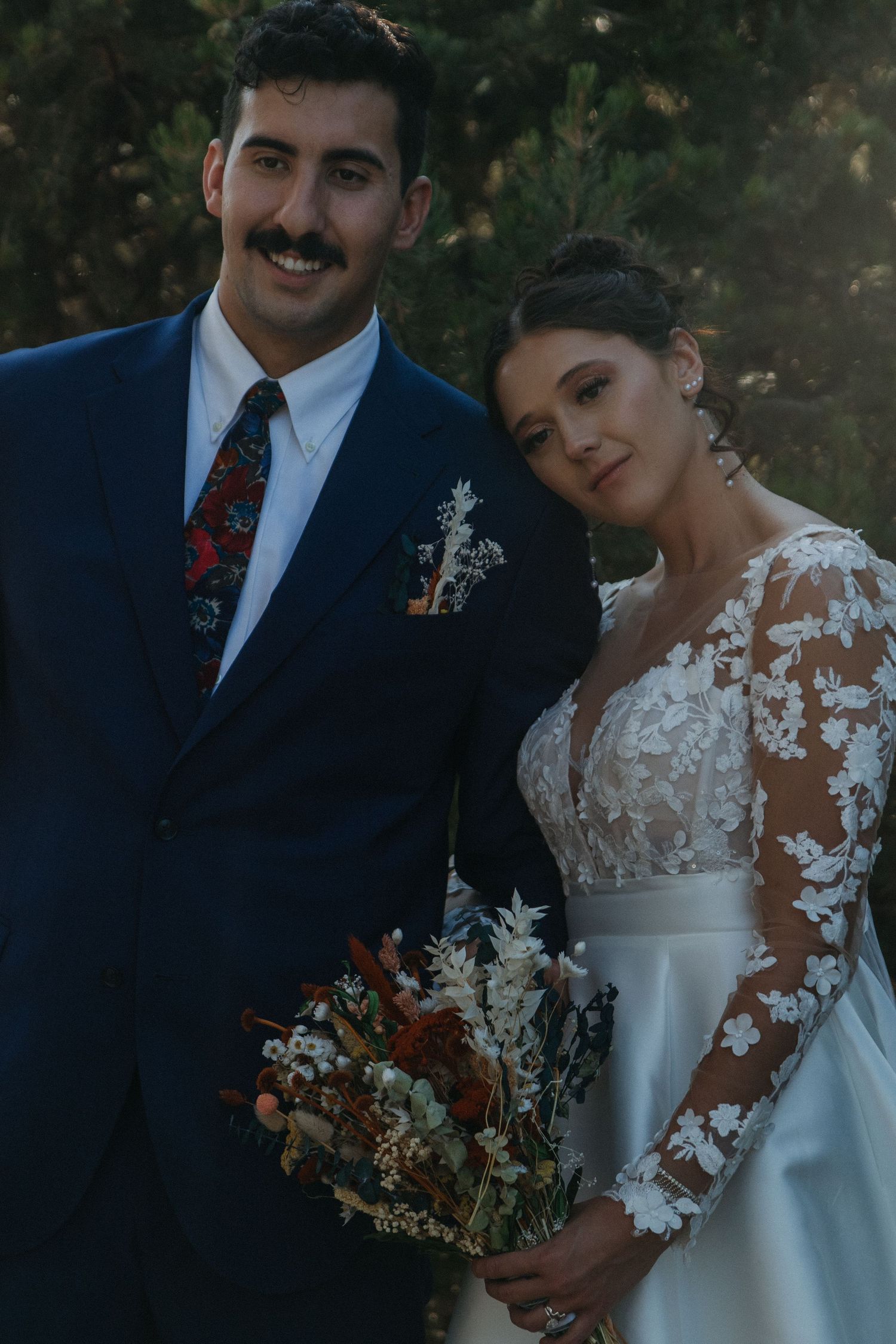 Couple poses for romantic wedding portraits in elegant attire at sunset.