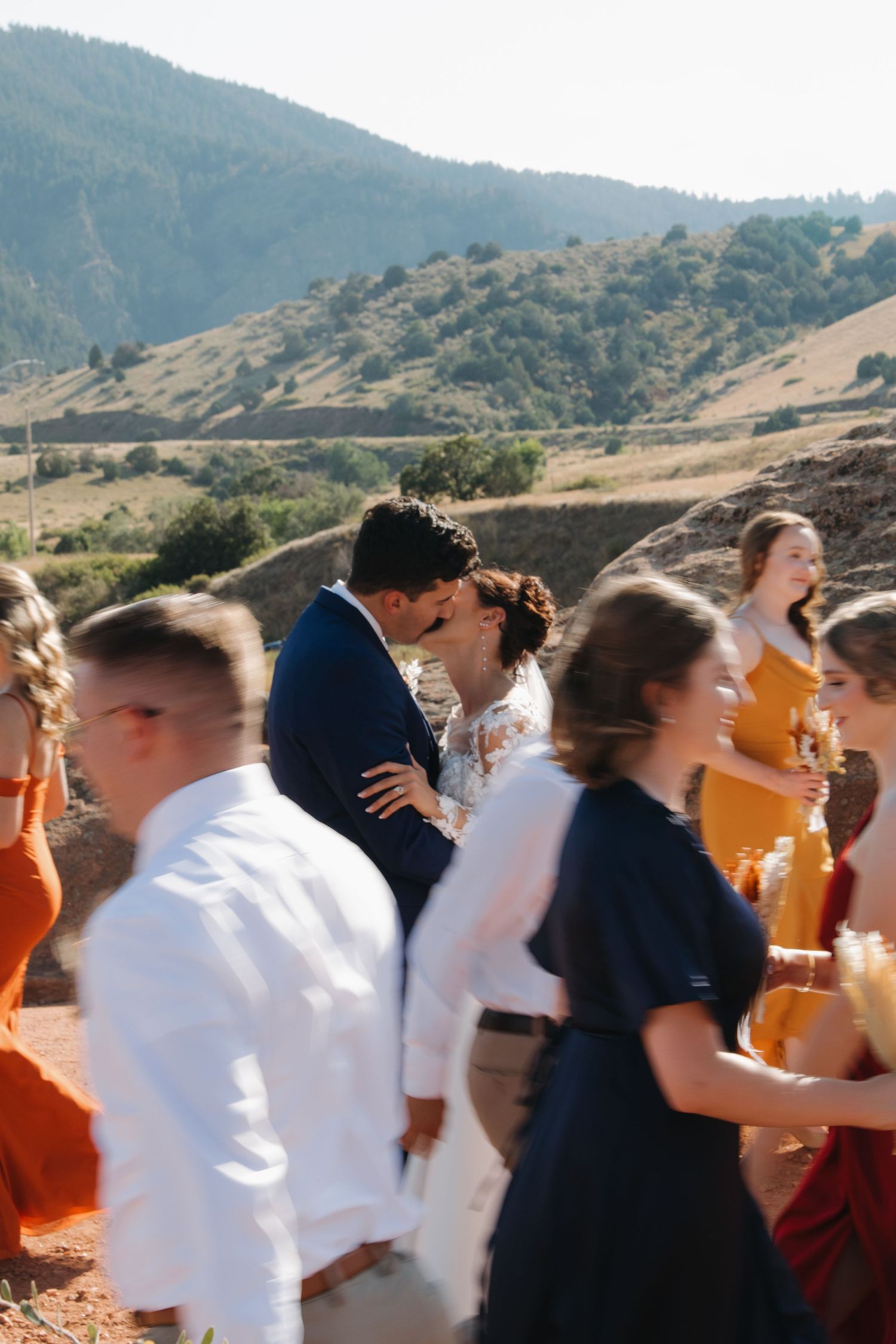 Wedding party in motion during celebratory moment against mountainous landscape.