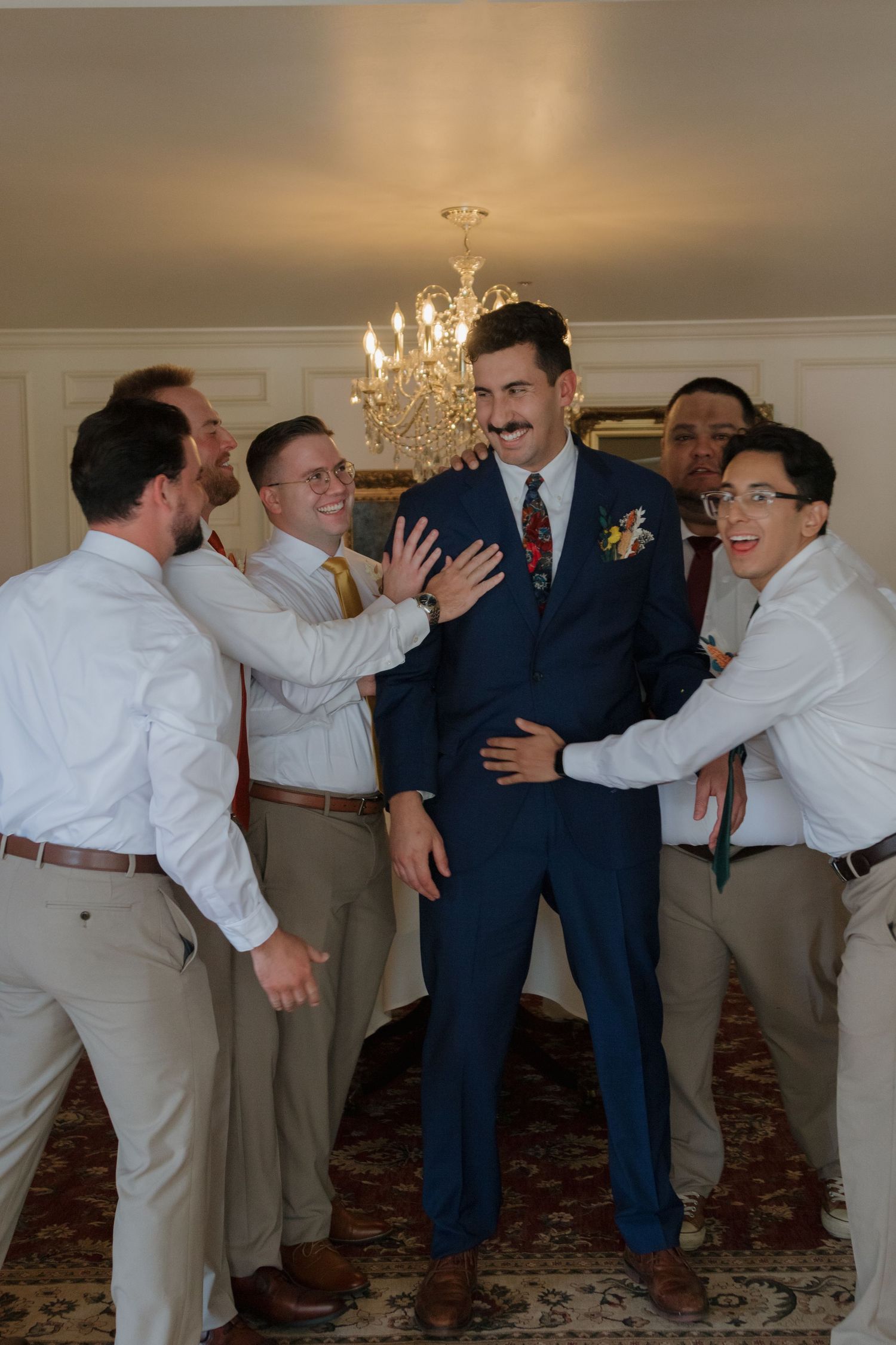 Groomsmen in navy suits and white attire perform a playful pushing sequence at a wedding venue.
